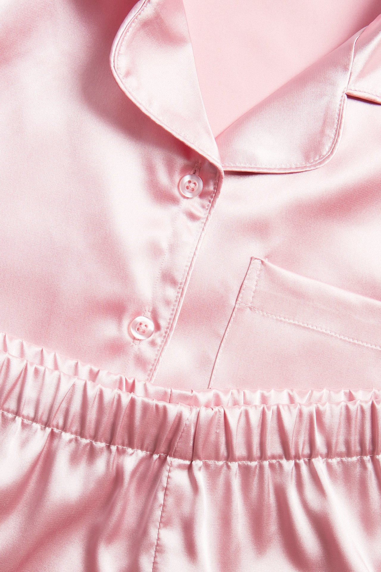 Zbliżenie jasnoróżowej satynowej piżamy z kołnierzykiem, guzikami, kieszenią i elastycznym pasem.