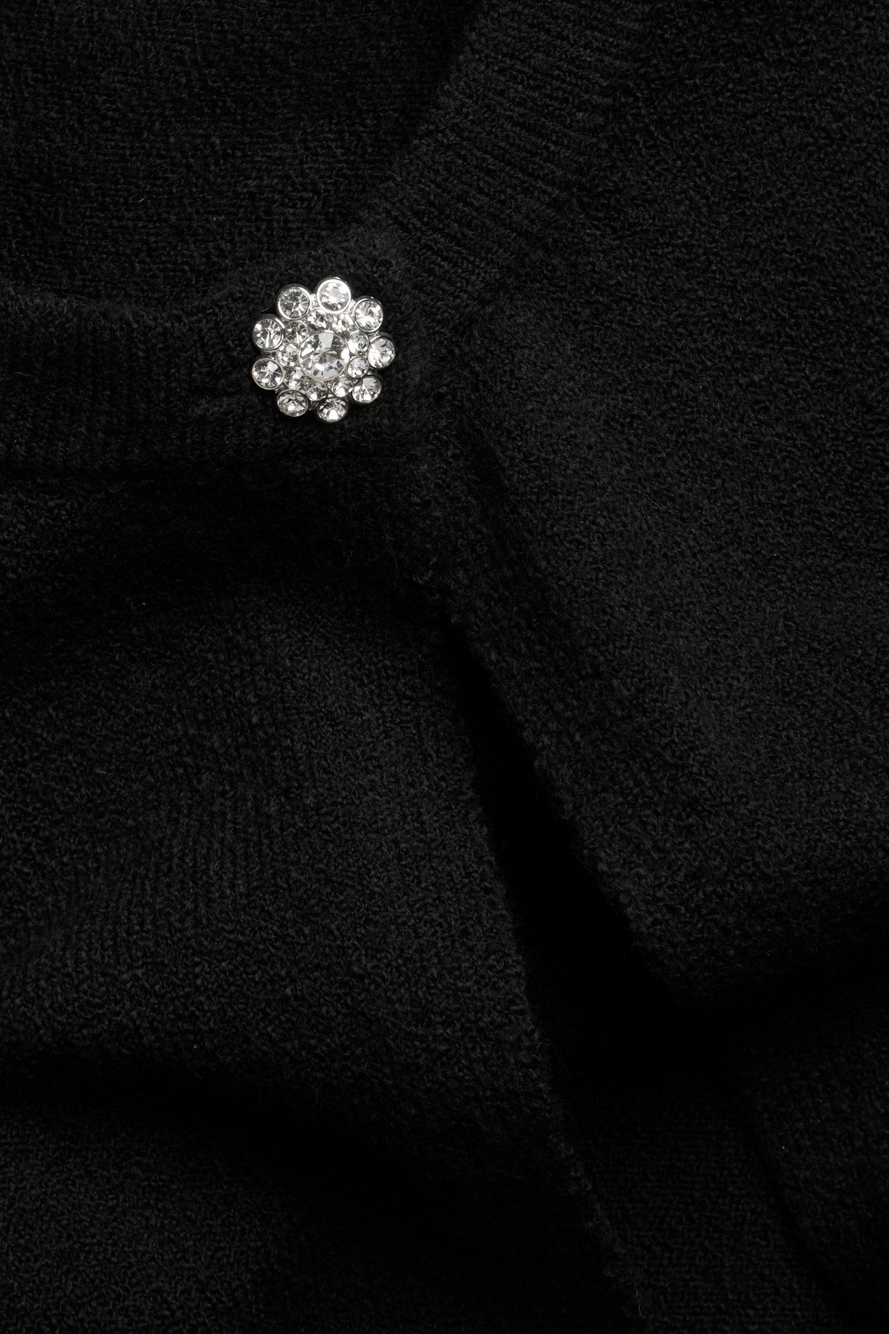 Zbliżenie czarnego dzianinowego kardiganu z błyszczącym, okrągłym guzikiem z dżetów.