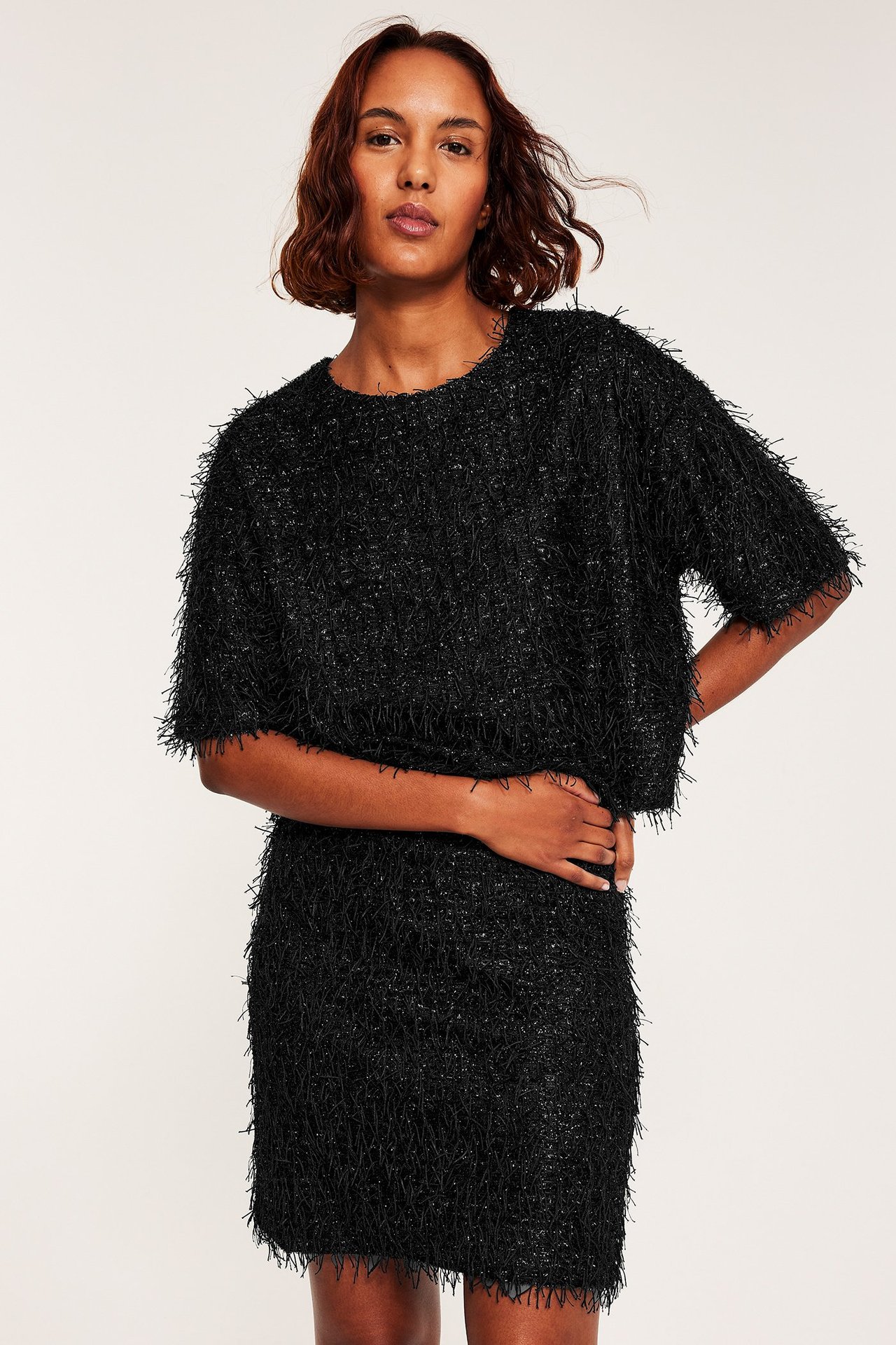 Dammodell i svart linne och kjol med fransar, over en mörk top, fransar och skrynklig textur.