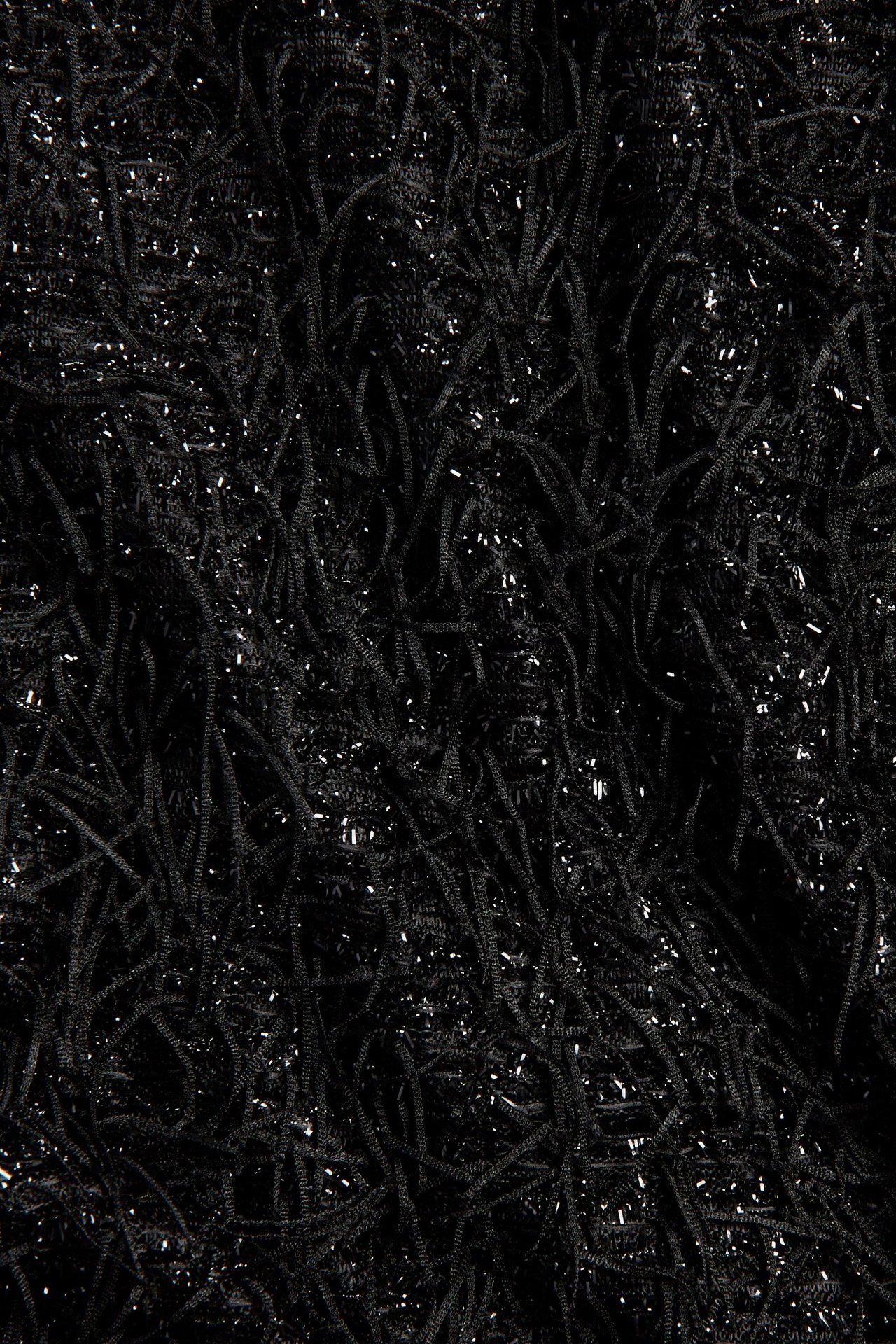 Zbliżenie na czarny materiał spódnicy z frędzlami i srebrnymi cekinami.