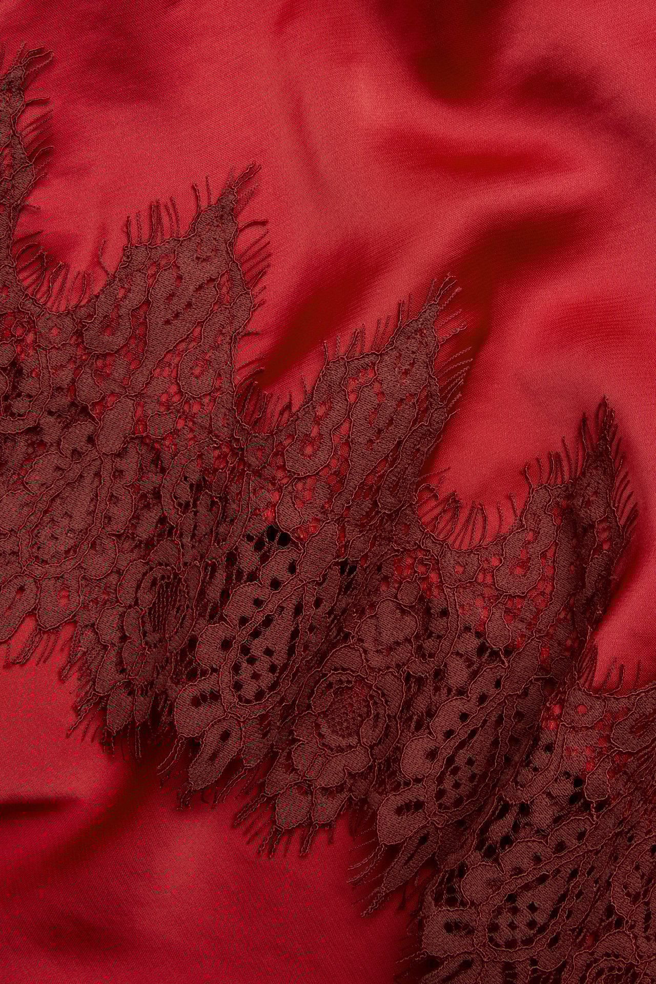 Zbliżenie na czerwoną tkaninę spódnicy z ciemnoczerwoną koronkową lamówką w kwiaty.
