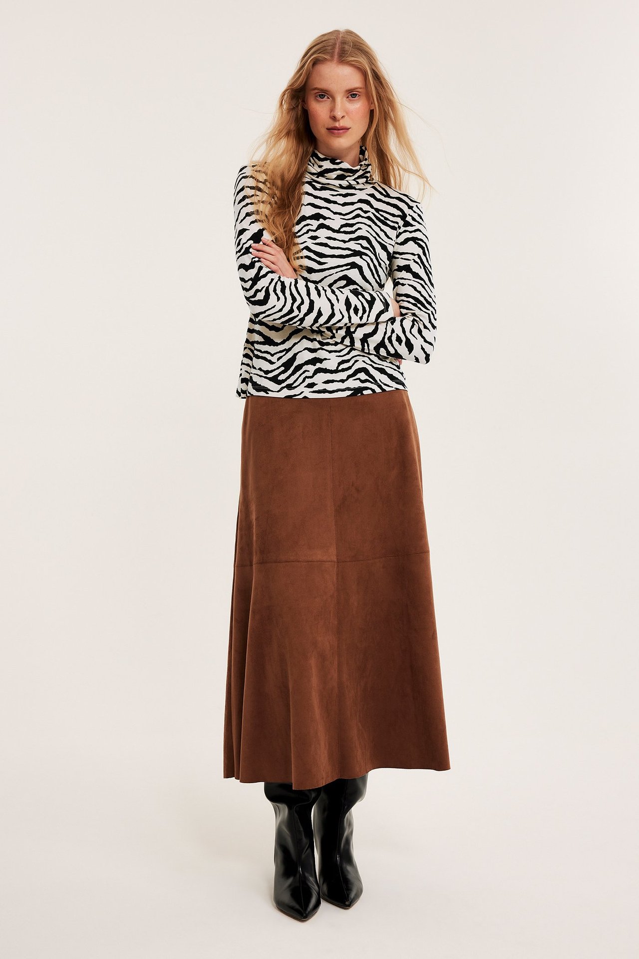 Kvinne i sebra-mønstret viskose turtleneck, brunt maksiskjørt og svarte støvler. Frontvisning.
