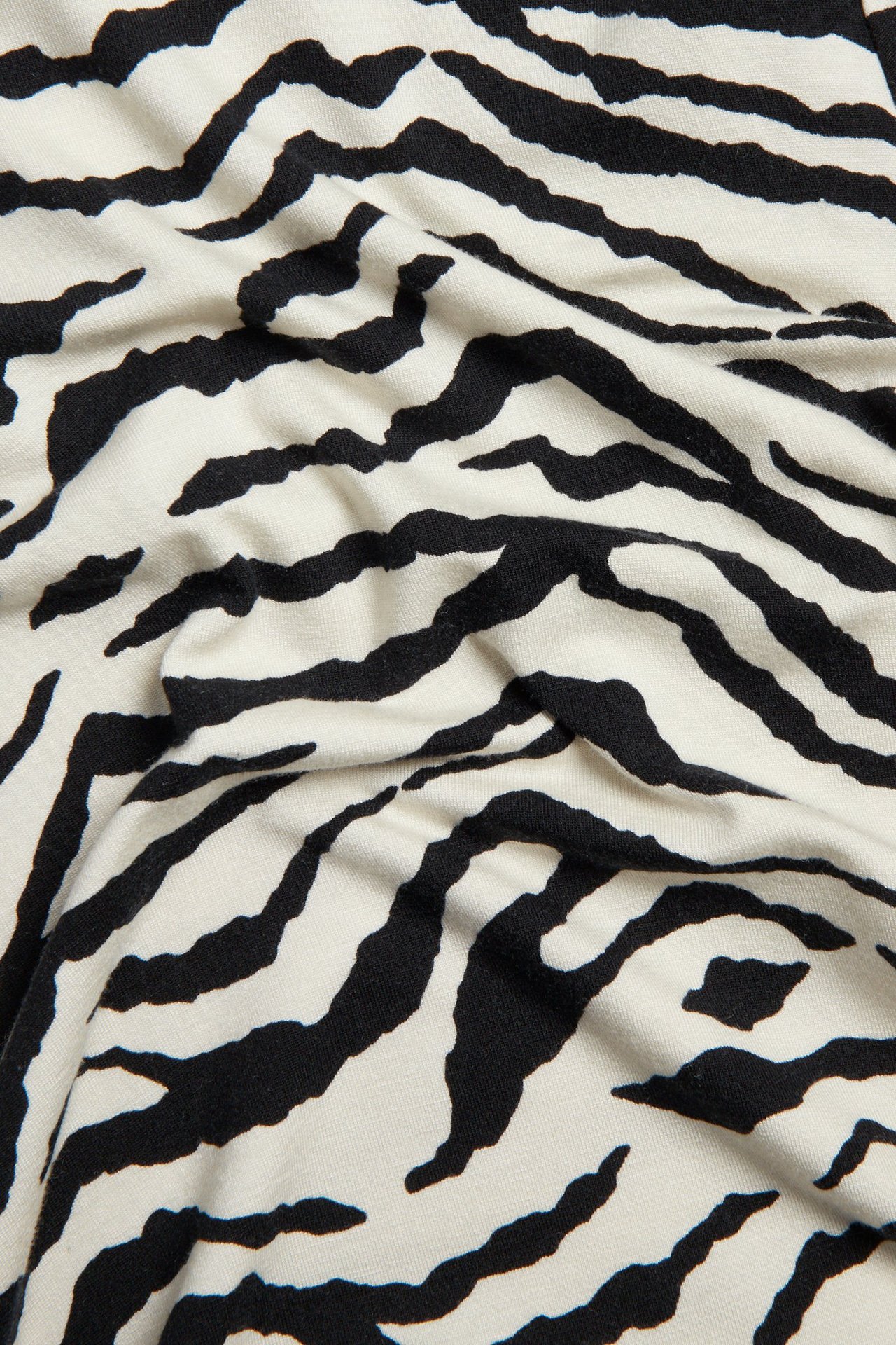 Zbliżenie czarno-kremowego, wiskozowego materiału w zebrę, na bluzkę z długim rękawem.