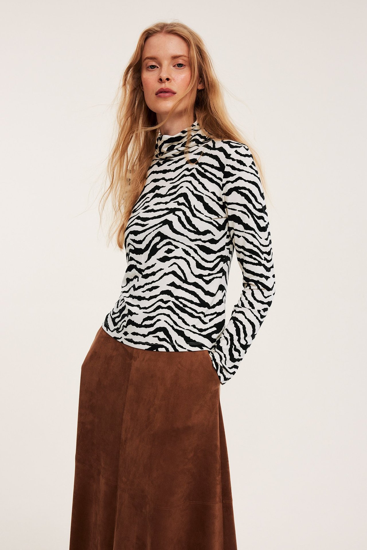 Widok z przodu kobiety w dopasowanym czarno-białym topie w zebrę z golfem i brązowej spódnicy midi.