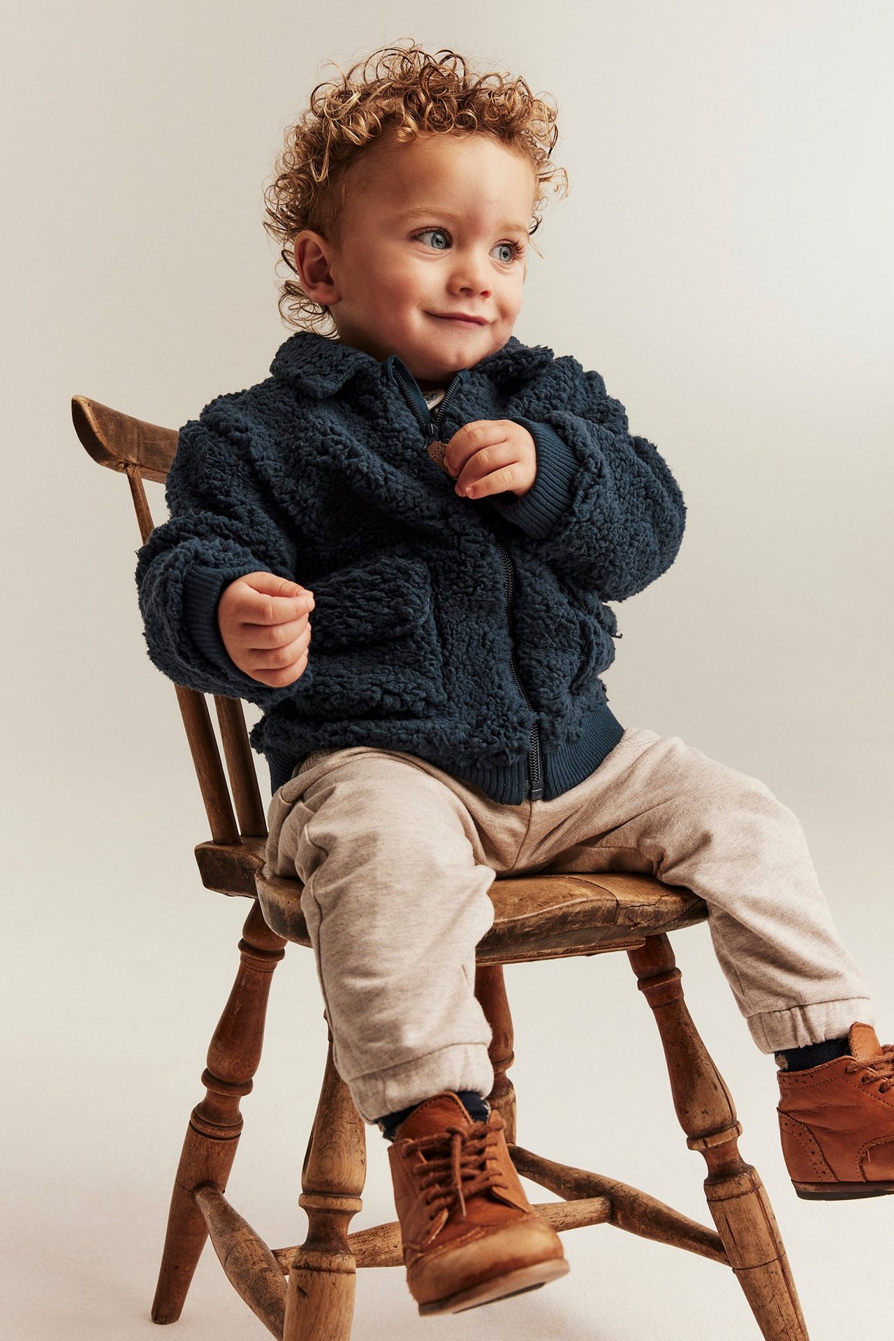 Frontvisning: Baby har på en mørkeblå brodert pilejakke, lysebeige bukser og brune sko.