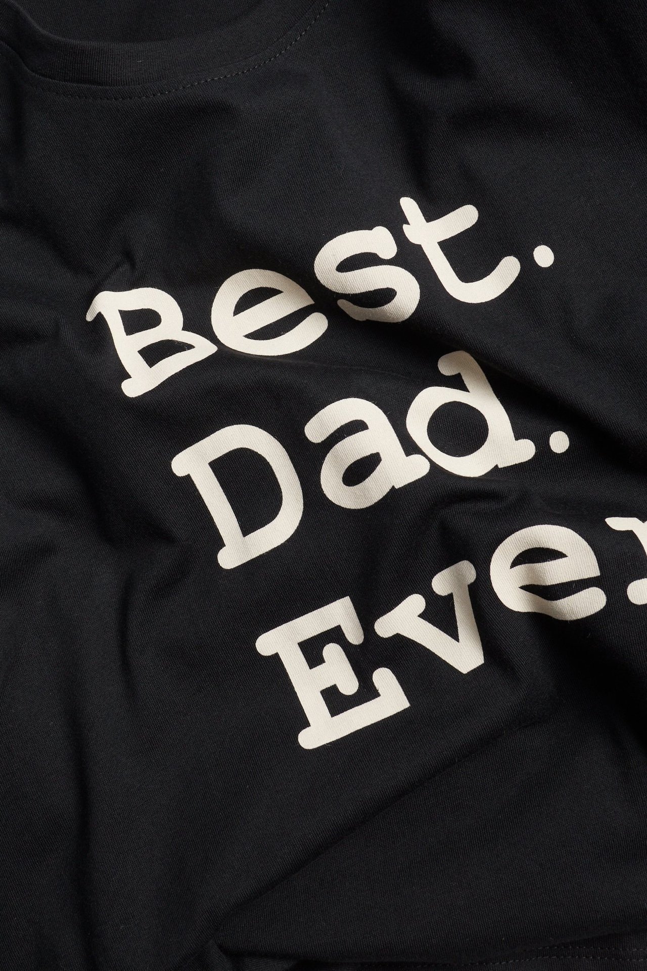 Zbliżenie na czarny bawełniany t-shirt z białym napisem 'Best. Dad. Ever.' z przodu.