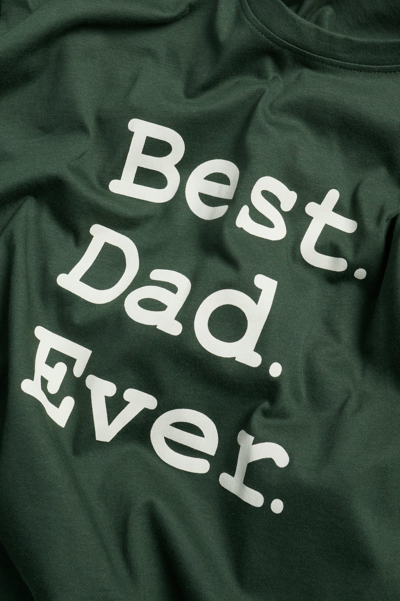 Zbliżenie z przodu zielonej bawełnianej koszulki z białym napisem 'Best Dad Ever.'.
