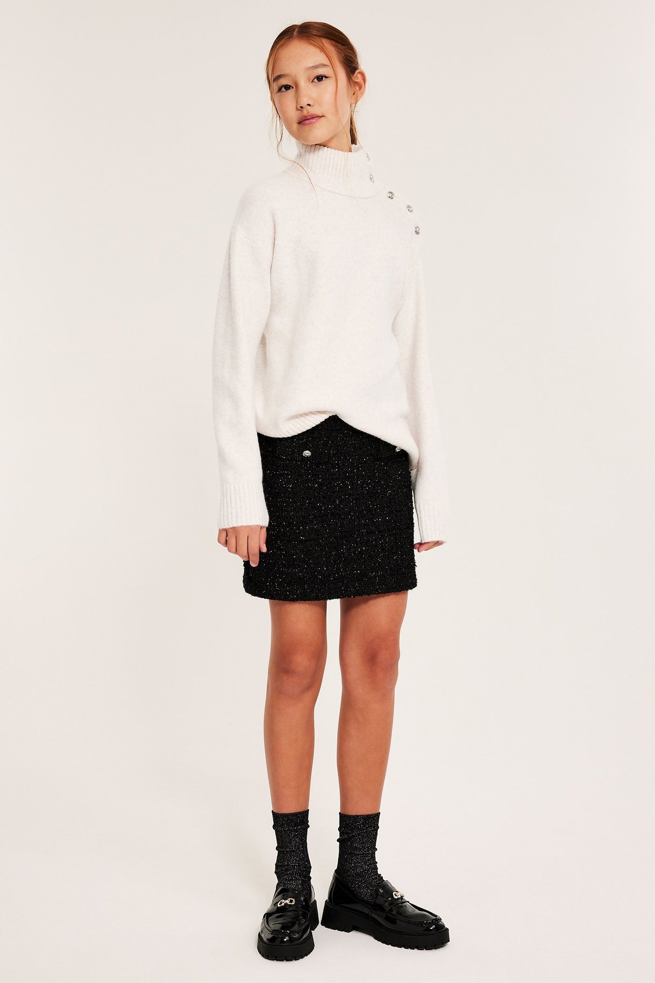 Biała dzianinowa polo z kołnierzem, ozdobne guziki, na czarnej spódnicy.