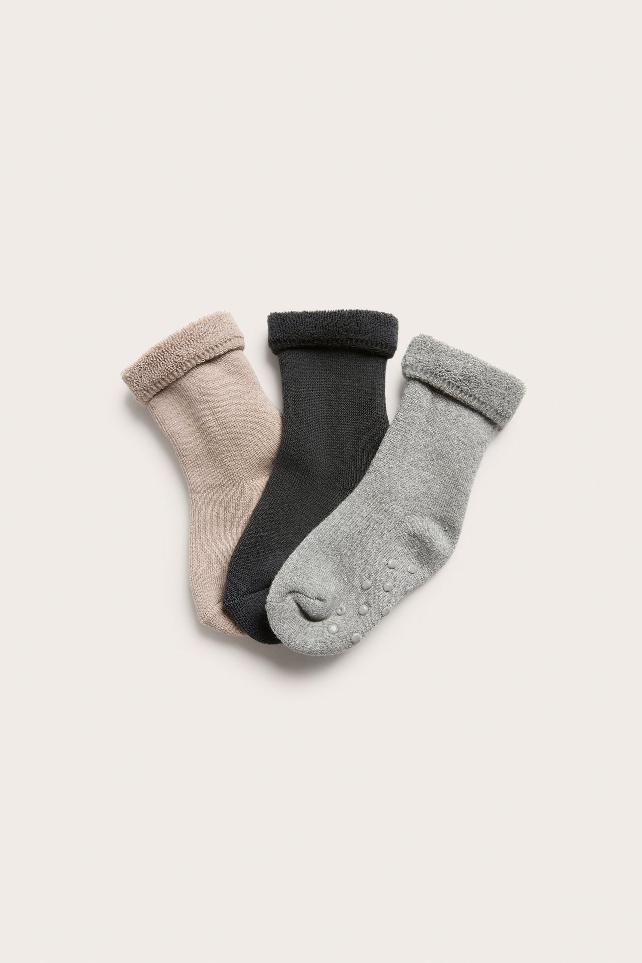 Topputsikt av 3-pakning babyfrotéstrømper i beige, mørk grå og lys grå med antiskliprikker.
