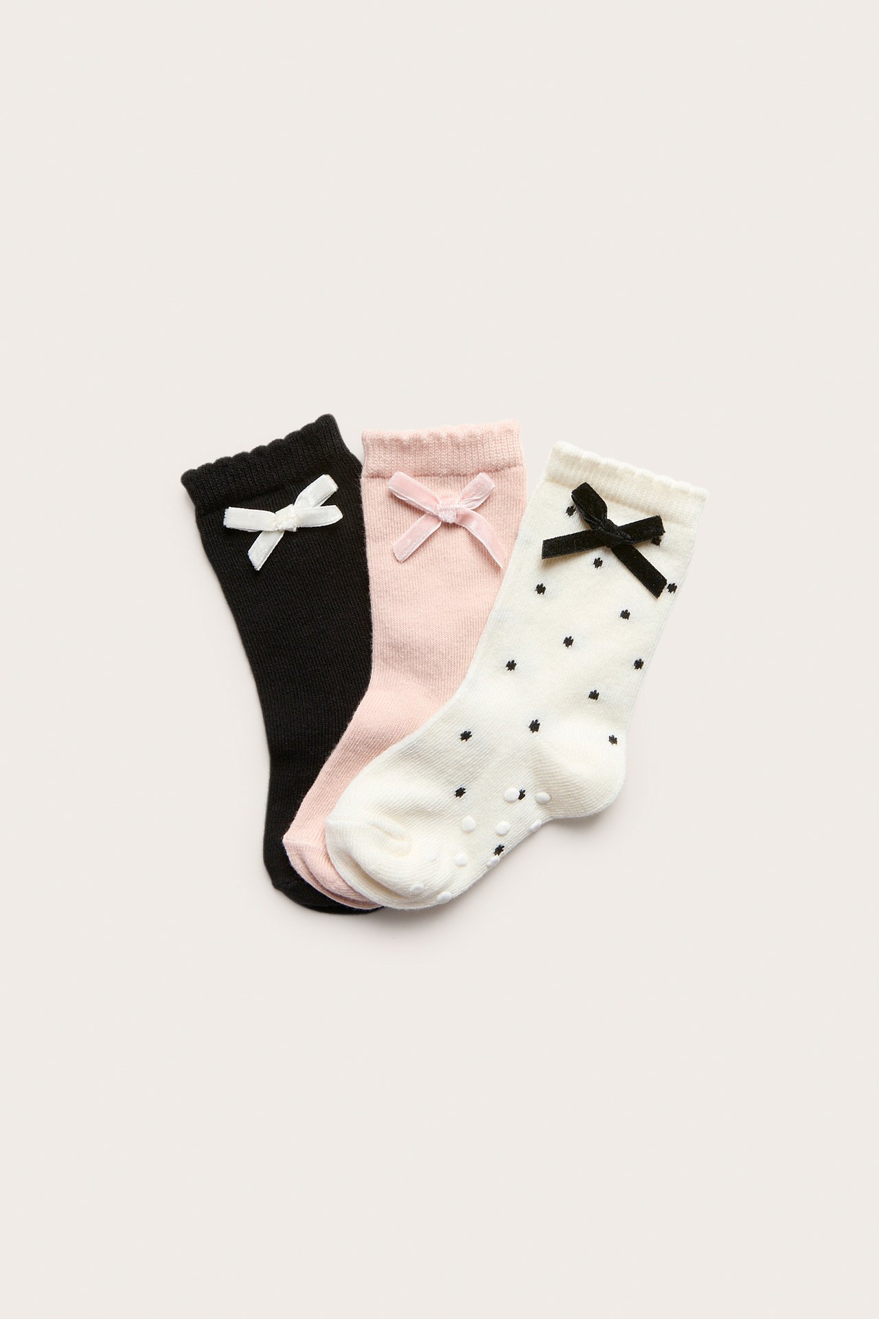 Toppbilder av tre babysokker med bølgekant og sløyfer: mønstret offwhite, rosa og svarte.