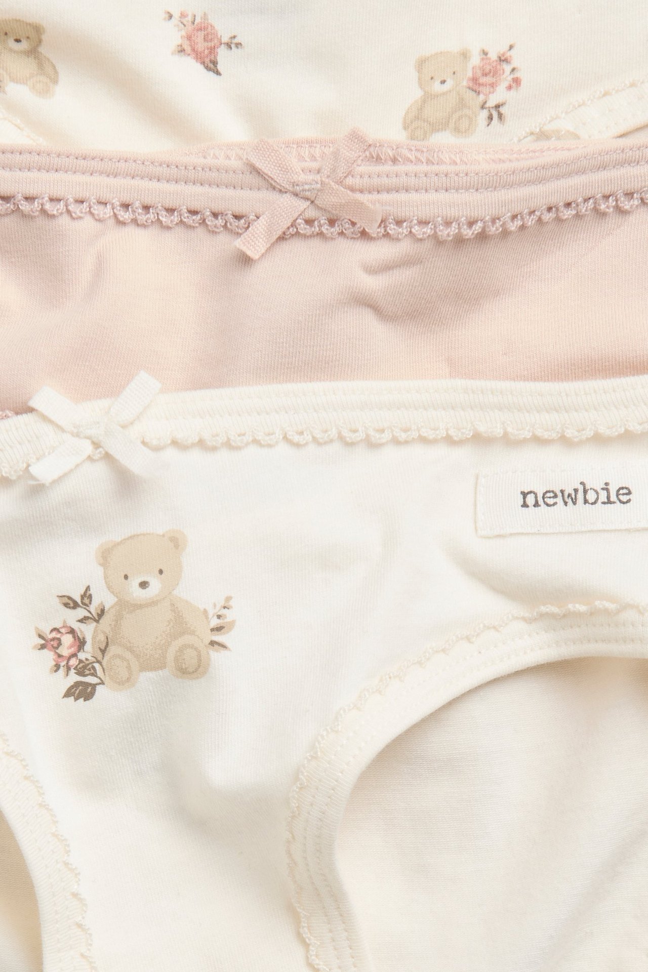 Nærbilde av tre par barnetruser i trikot: én rosa, to offwhite med bjørne- og blomstermønster.