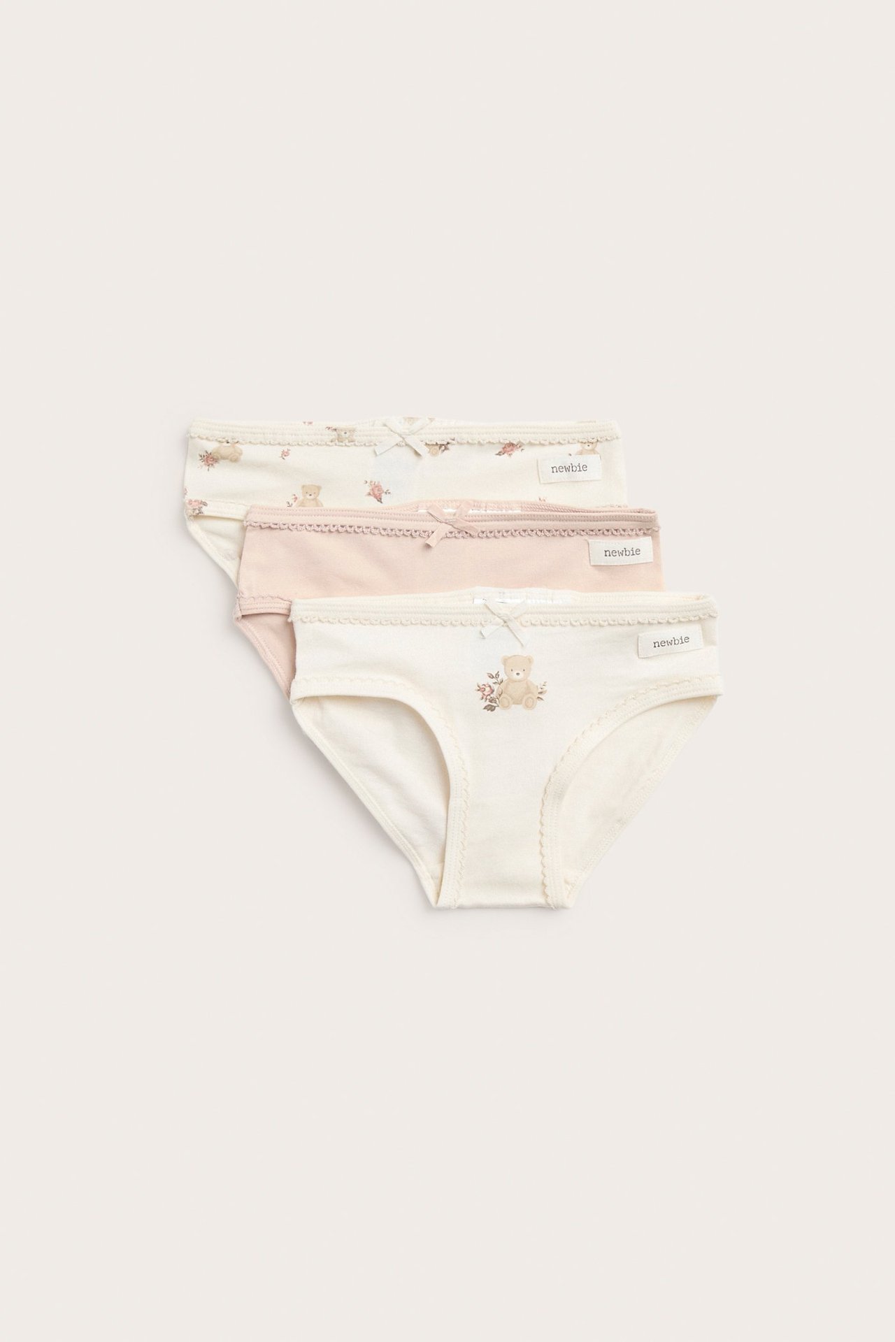 Frontvisning: tre par barnetruser i offwhite og rosa, to med blomster- og bjørnetrykk.