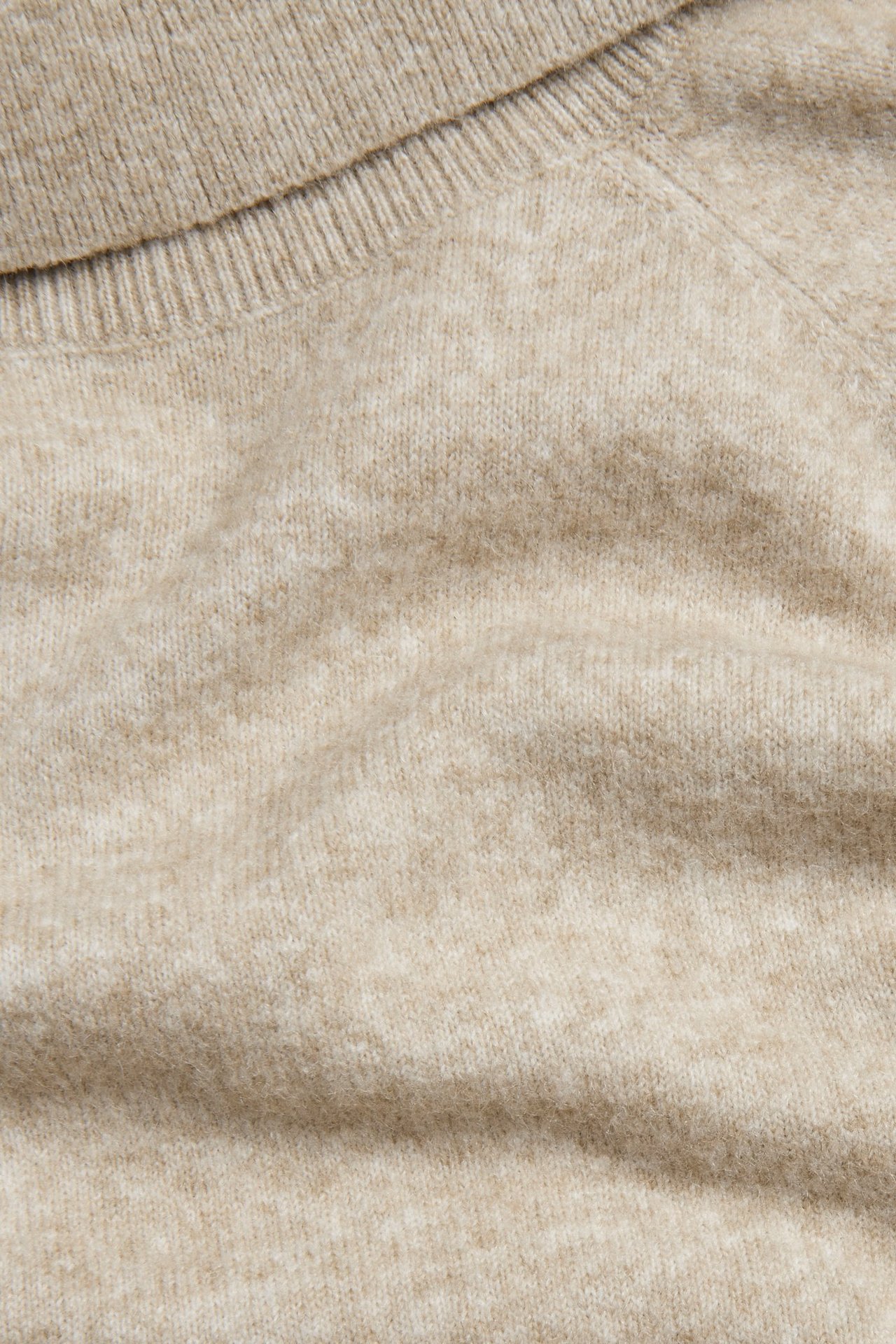 Zbliżenie beżowego, melanżowego swetra z dzianiny z golfem.