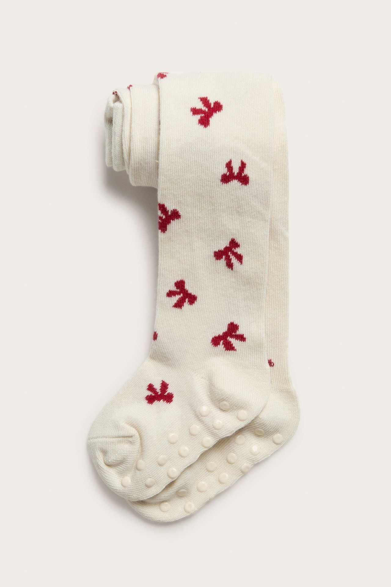 Widok z góry na złożone, ecru rajstopy niemowlęce w czerwone kokardki z antypoślizgowymi podeszwami.