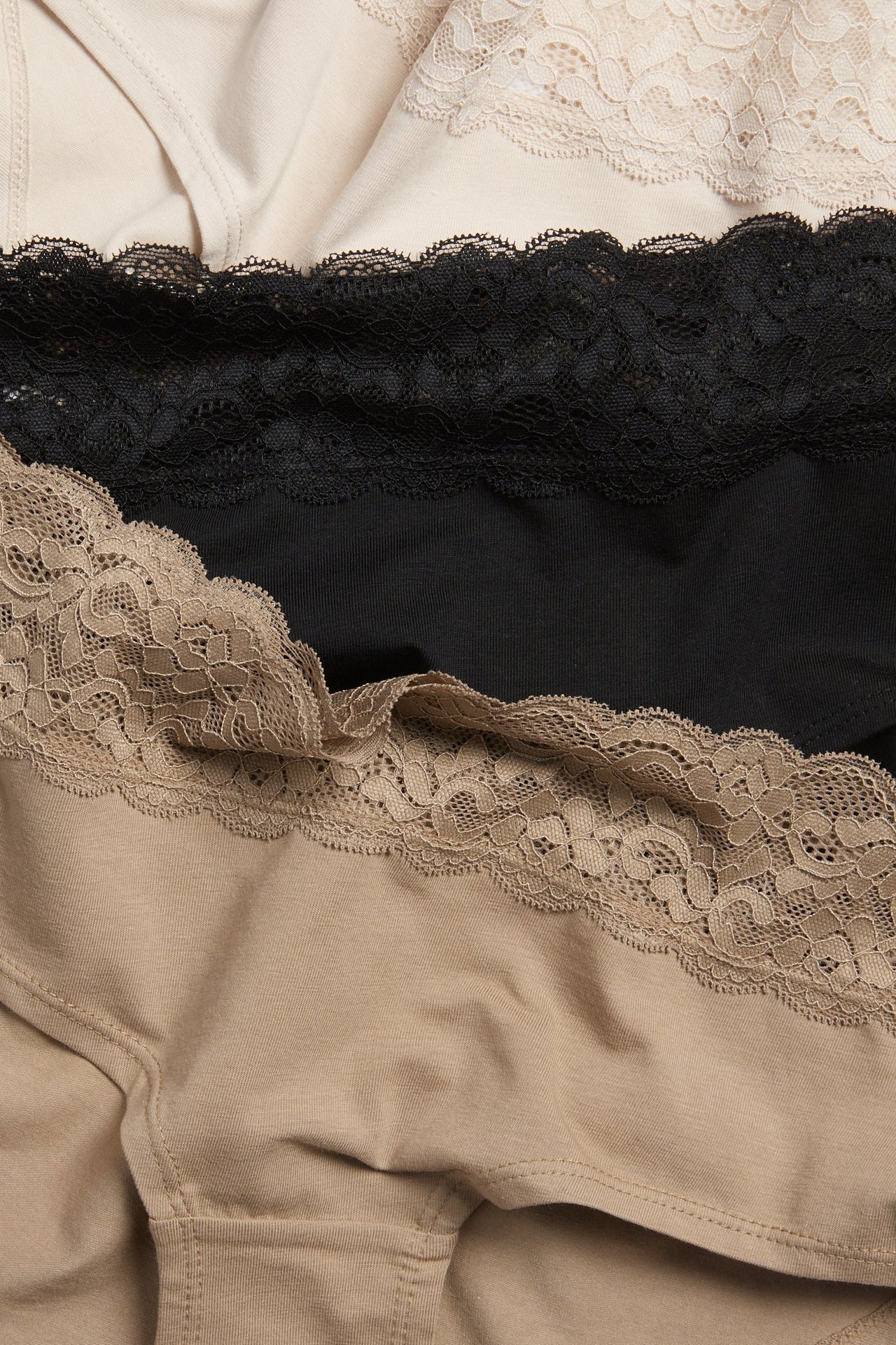 Widok z góry na trzy damskie figi typu hipster: jasnobeżowe, czarne i ciemnobeżowe, wszystkie z koronką.