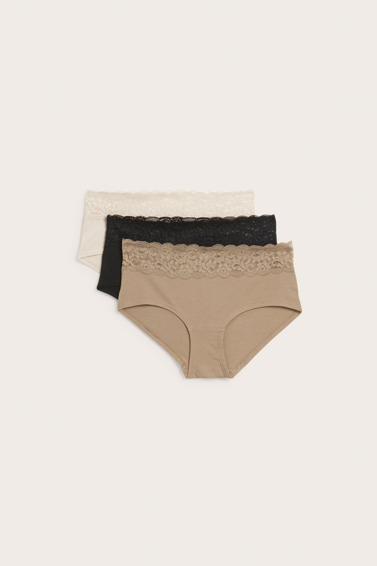 Ovenfra, tre stablede hipster-truser i bomullsblanding: beige, svart og off-white, alle med blondekant.