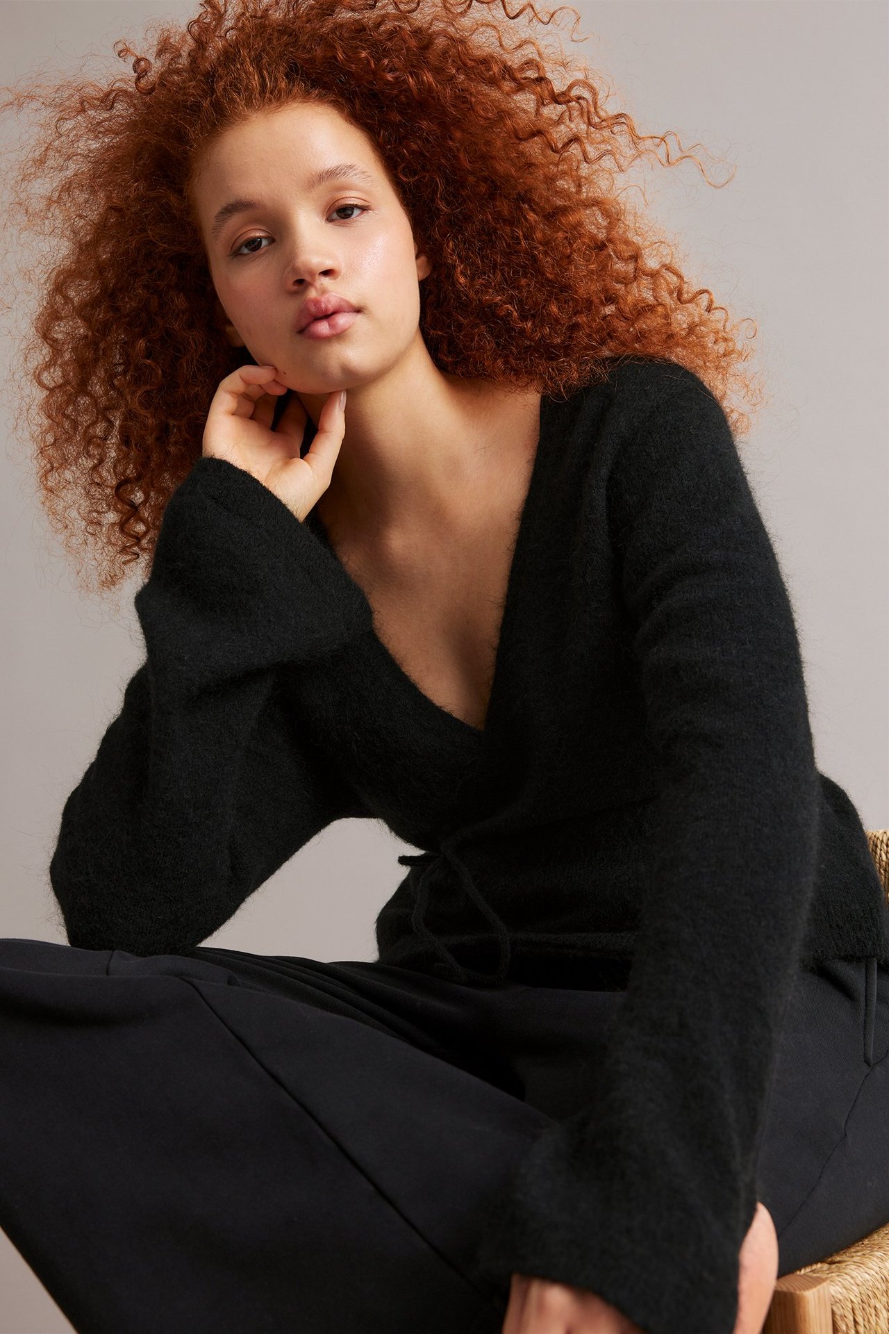 Widok z przodu: Kobieta w czarnym cienkim wełnianym kardiganie kopertowym z szerokimi rękawami i czarnych spodniach.