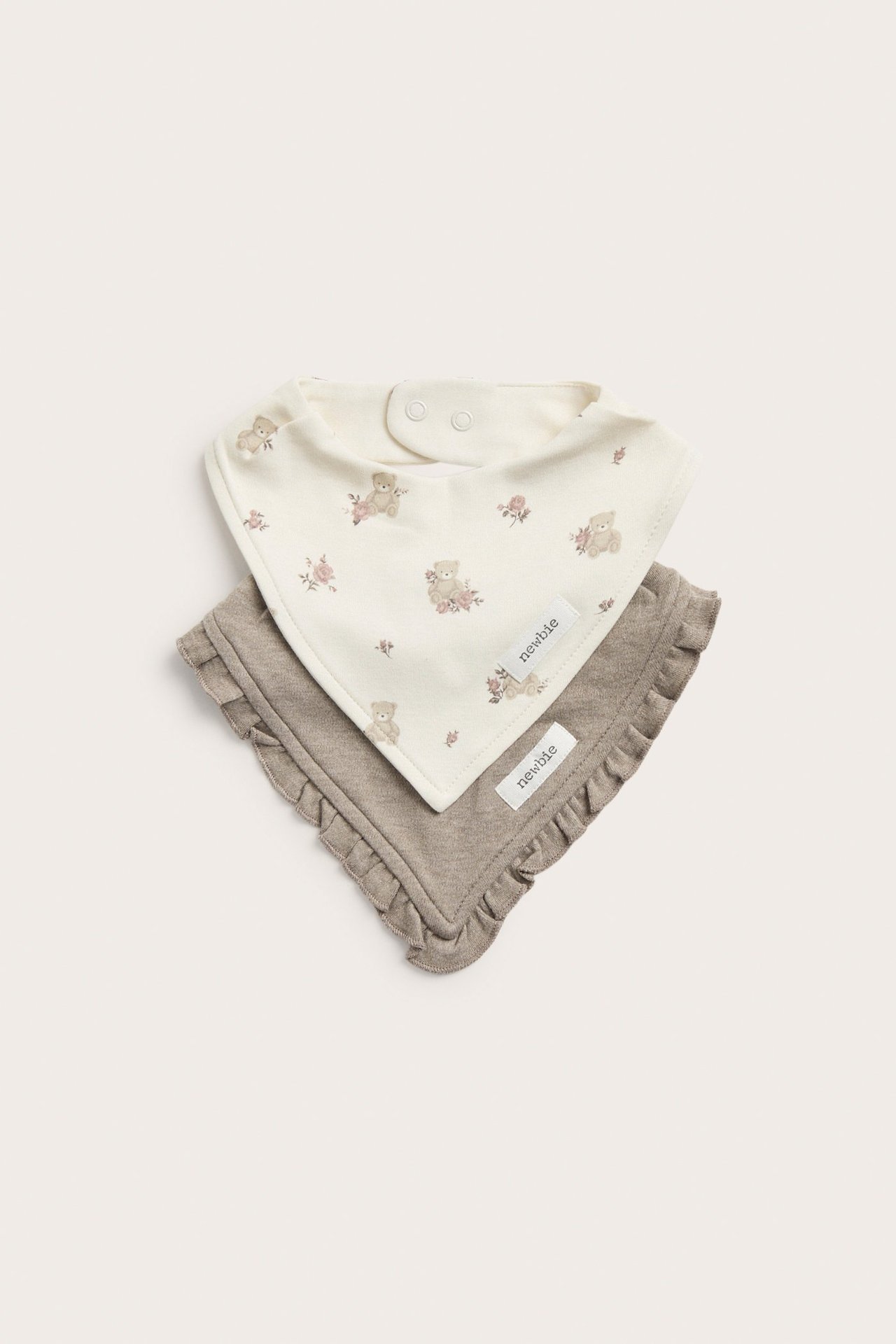 To baby bandana-smekker: en offwhite med bamse- og blomstermønster, en ensfarget brun med volanger.
