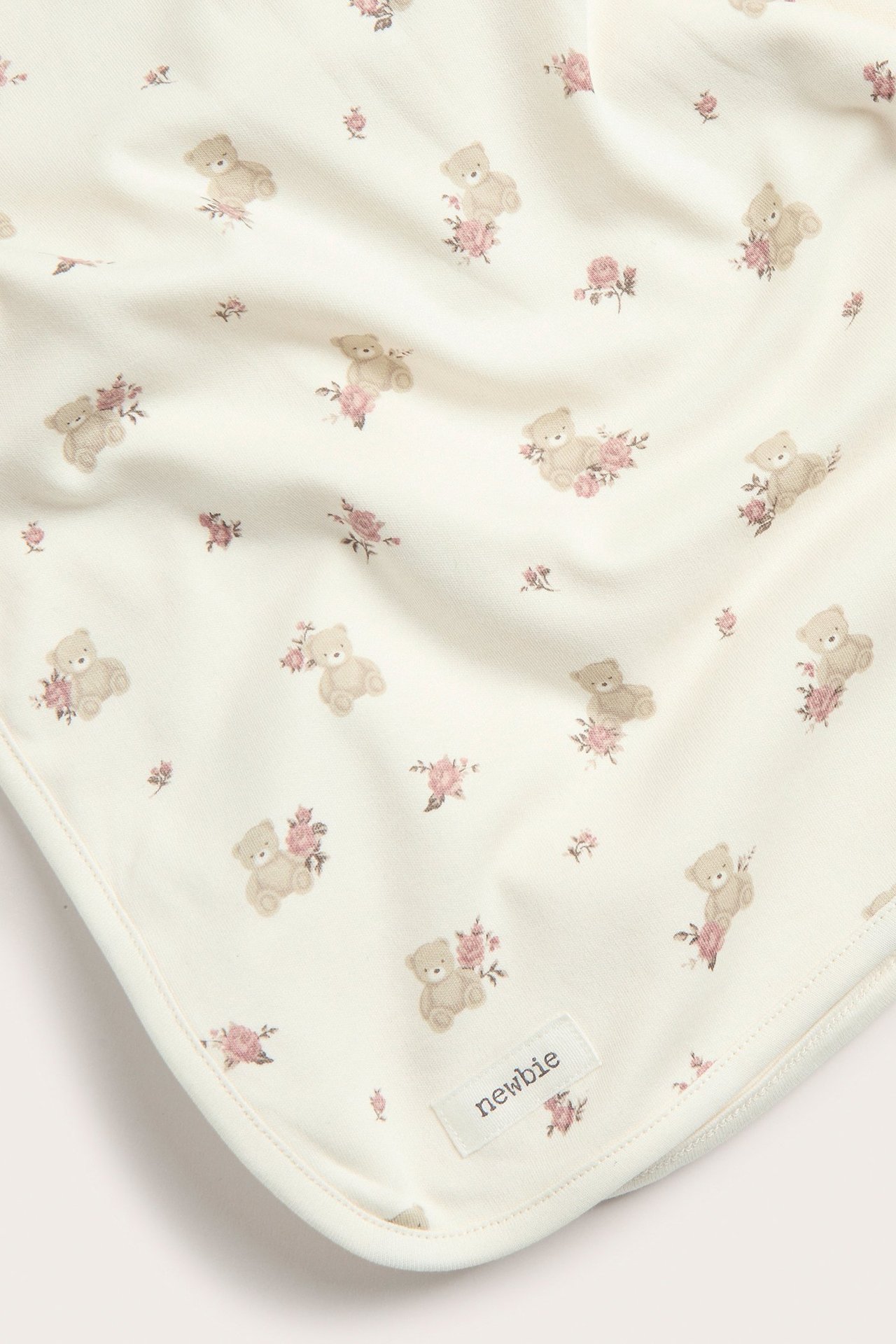 Lähikuva luonnonvalkoisesta puuvillaisesta vauvanpeitosta, jossa on kukka- ja nallekuvio.