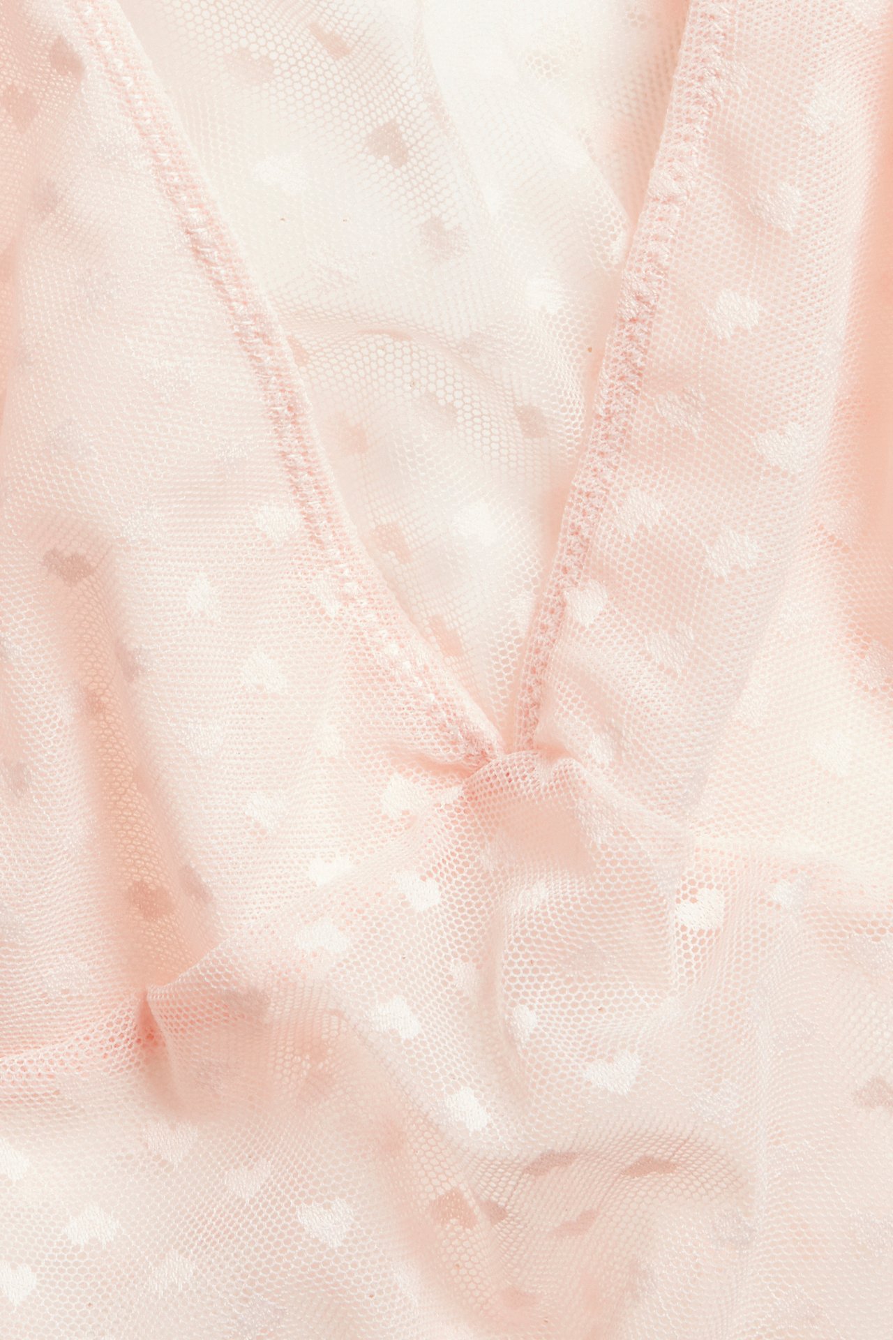 Nærbilde av en lys rosa mesh-topp med hjertemønster og V-hals.