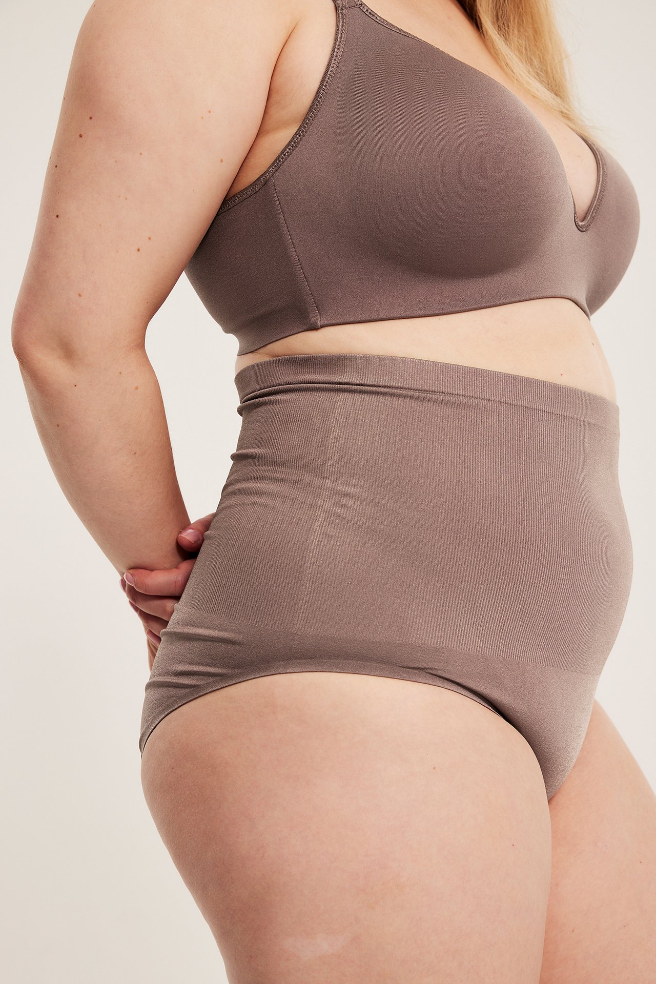 Sideprofil av en kvinne i en mauvefarget sømløs truse med høy midje og matchende BH.