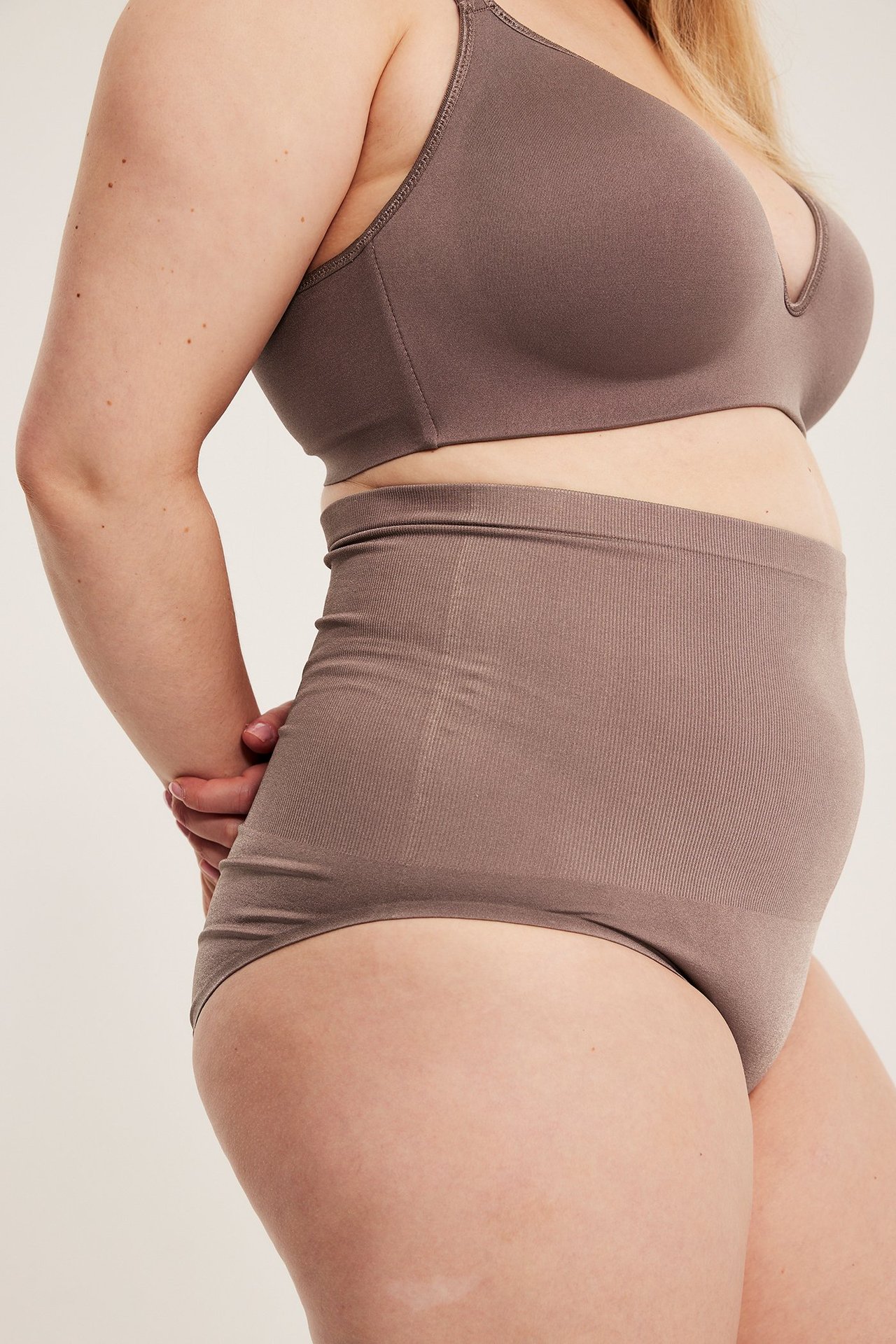 Widok z boku kobiety w bezszwowych majtkach z wysokim stanem w kolorze mauve i biustonoszu.