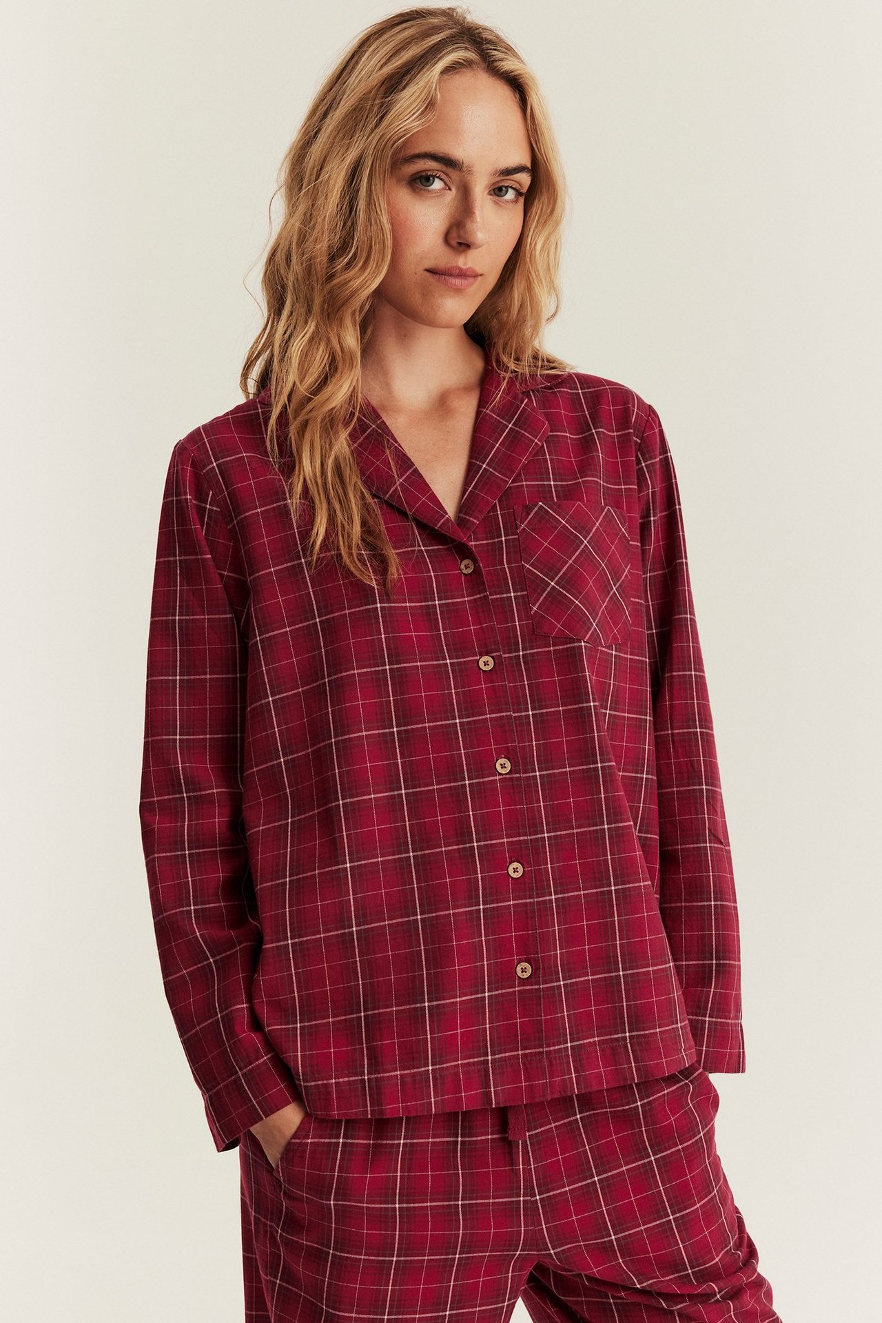 Frontbilde av en kvinne i rød rutete flanellpyjamas med krage, knappelukking foran og bukser.