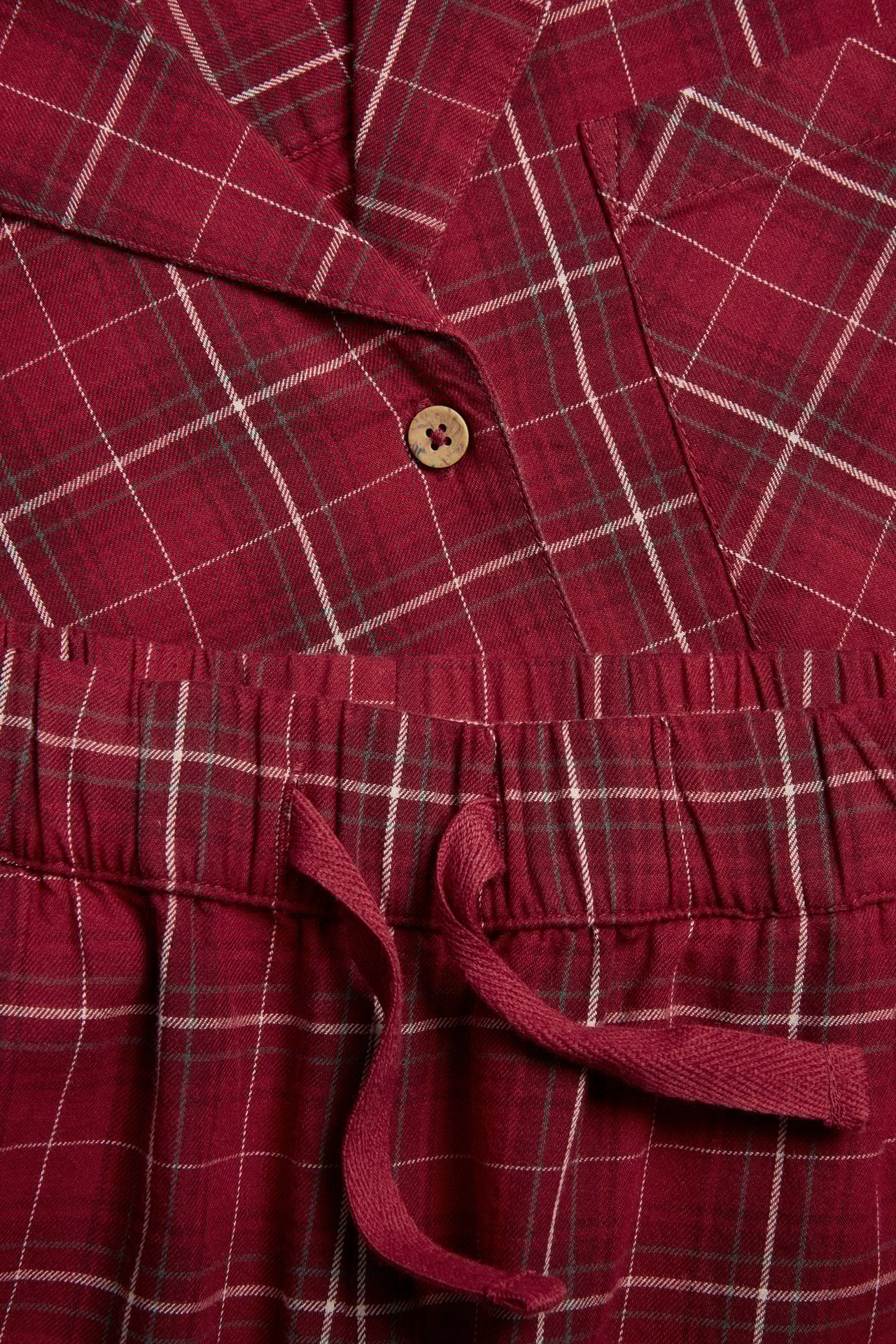 Nærbilde av en rutete flanellpyjamas for dame i rødt, med knappetopp og snøring i buksene.