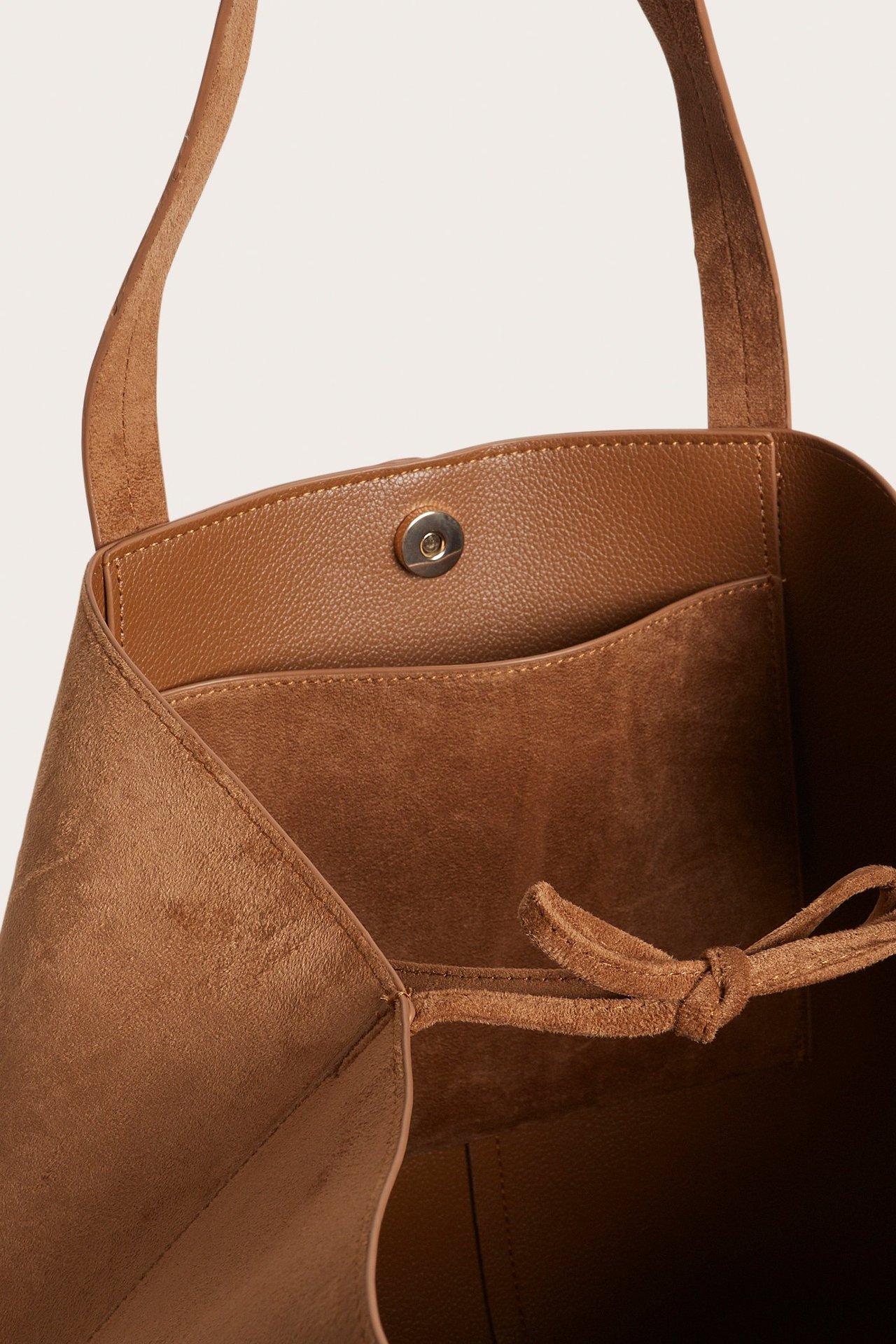 Zbliżenie brązowej torby tote z imitacji zamszu, zapięciem magnetycznym, kieszenią i paskami.