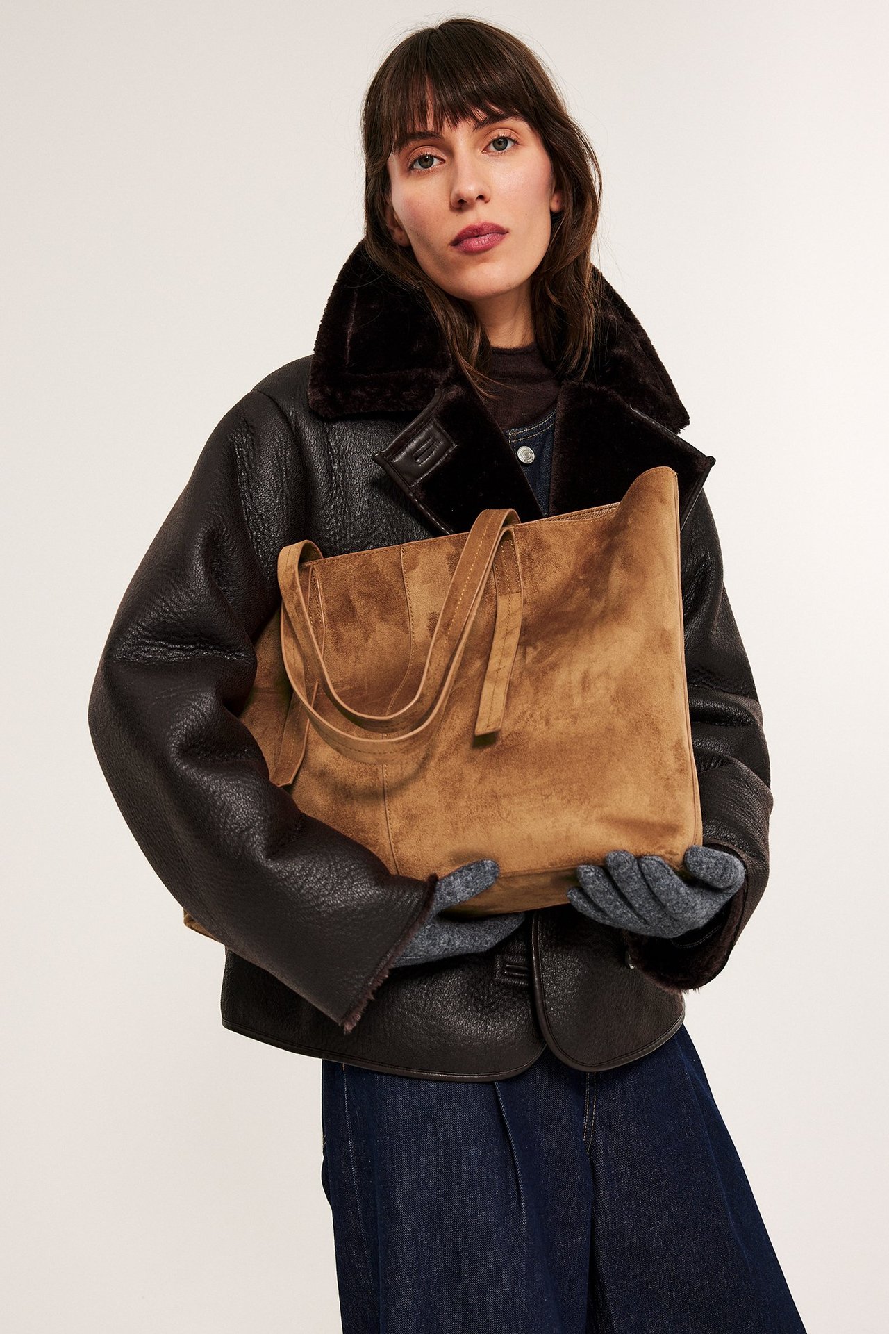 Kobieta w czarnej kurtce i szarych rękawicach trzyma brązową torebkę, widok z przodu.