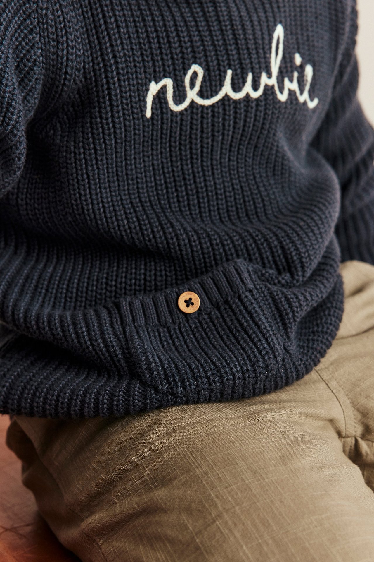 Barnets mörkblå stickade Newbie-tröja med vit brodyr, träknapp och khakifärgade byxor.
