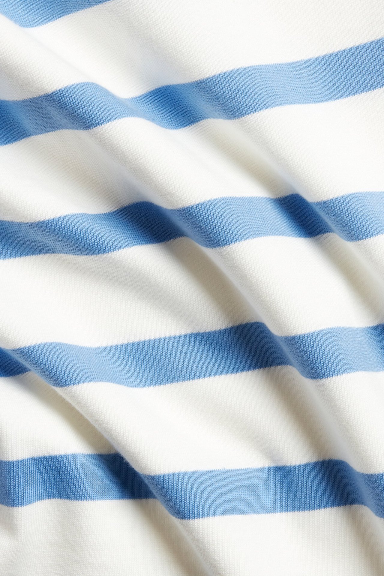 Zbliżenie na jasnoniebiesko-biały bawełniany materiał w paski z topu, z miękkimi fałdami.