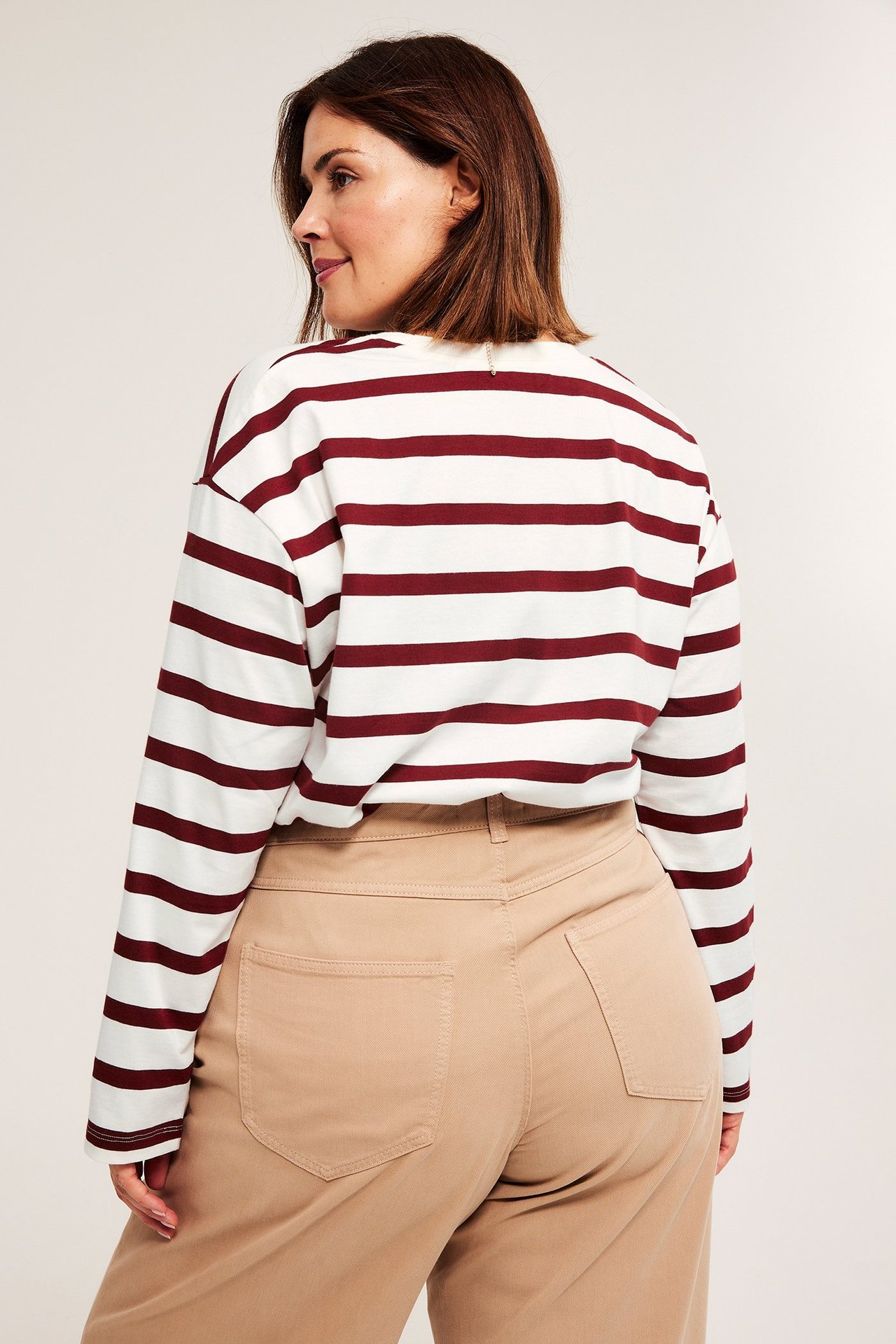 Baksidebilde av kvinne i rød- og hvitstripete langermet bomullstopp og beige bukser.