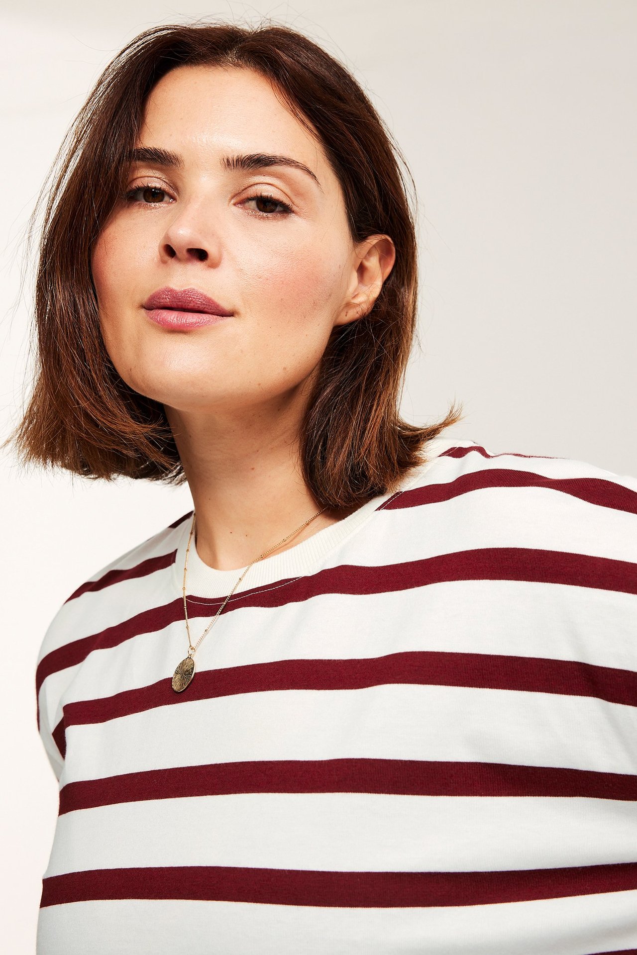 Forfra av en kvinne i rød- og hvitstripet topp og et gullfarget anhengskjede.