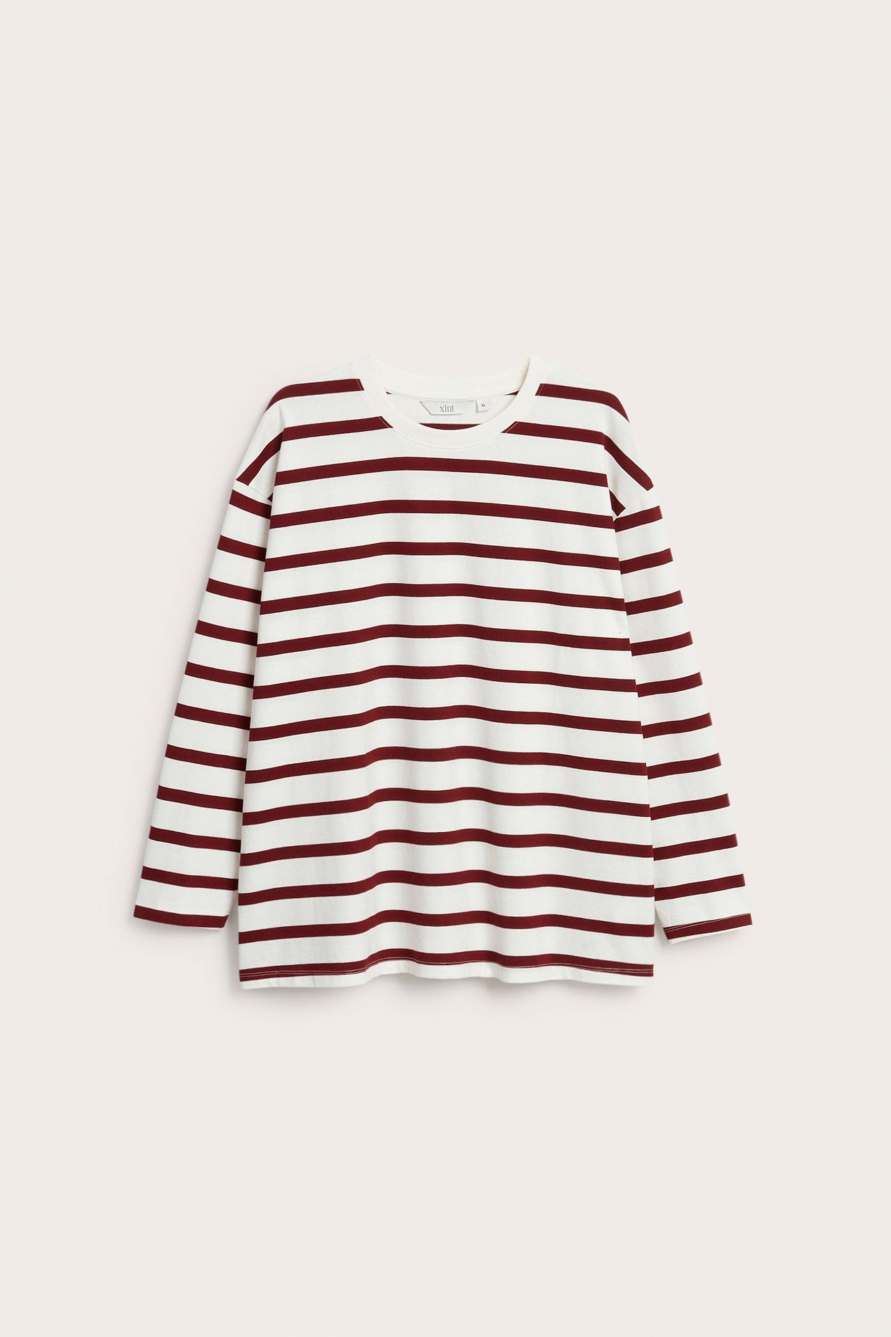 Framifrån: lös vit långärmad bomullstopp med röda horisontella ränder och rund hals.