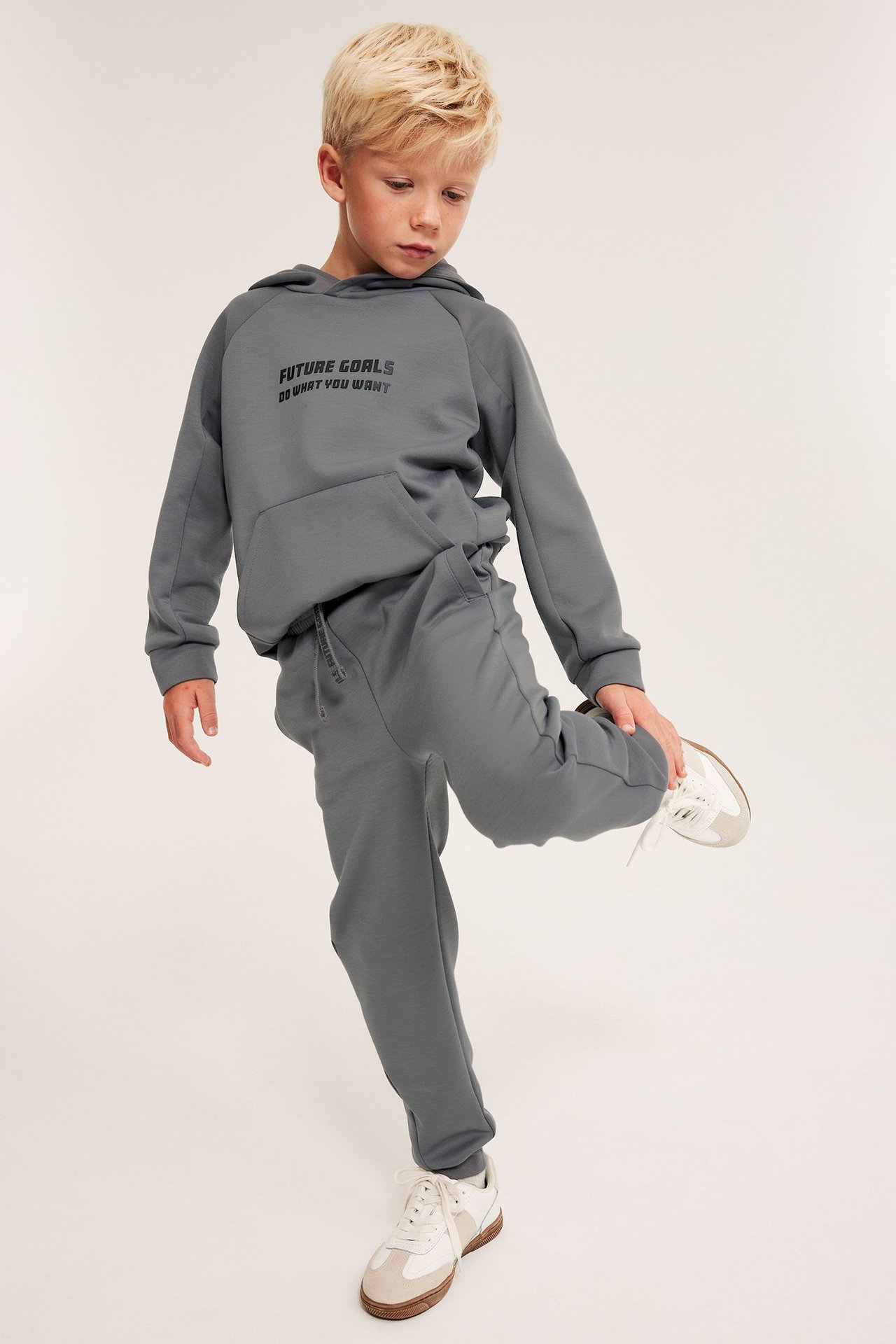Edestäpäin: lapsi harmaissa interlock-collegehousuissa ja harmaassa 'FUTURE GOALS' -hupparissa.