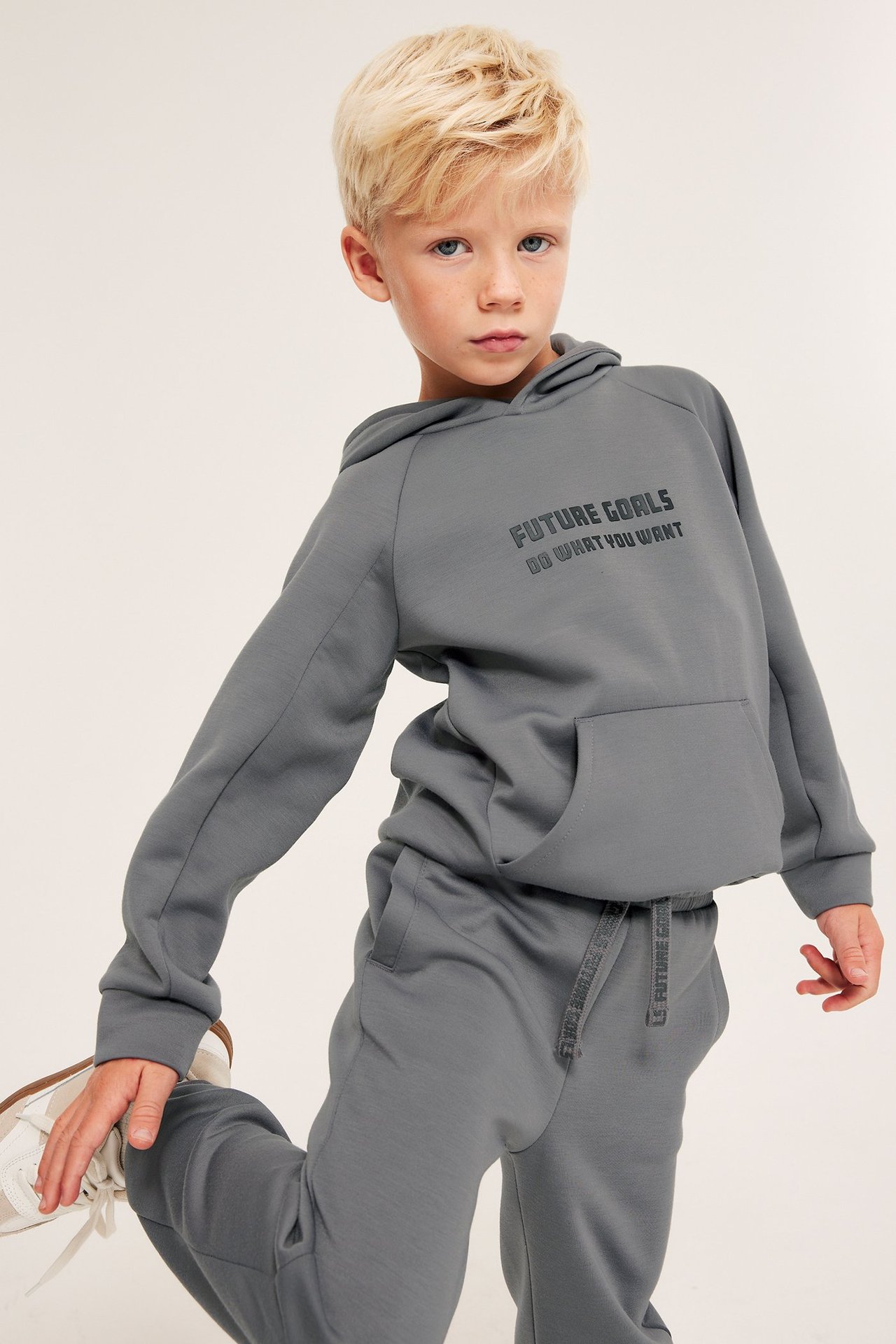 Widok z przodu dziecka w szarych spodniach dresowych z interlocku z nadrukowanymi sznurkami i pasującej bluzie.