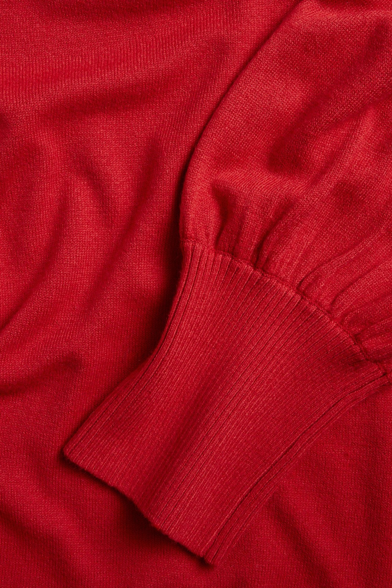 Zbliżenie na czerwony, dzianinowy rękaw sukienki z bufką i ściągaczem.