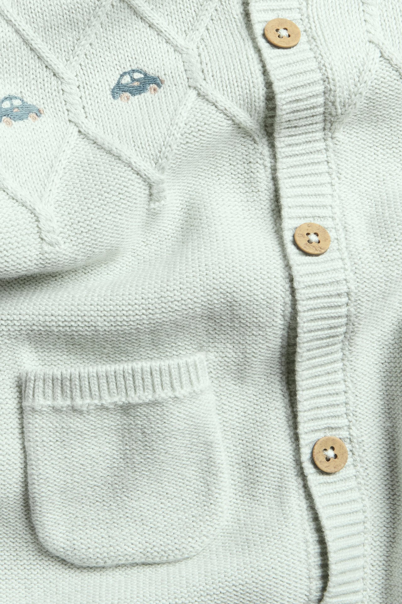 Jasnoniebieski, strukturalny kombinezon dziecięcy z haftem, guzikiem i ściągaczami przy dekolcie i rękawach.