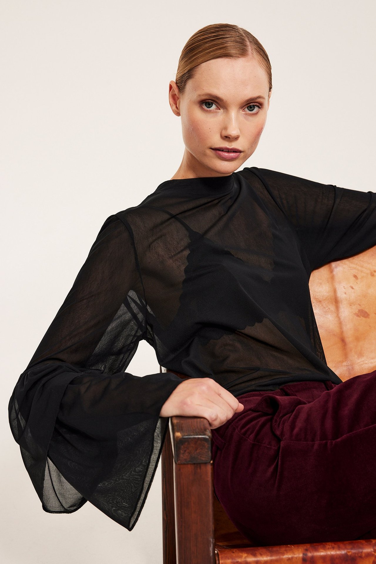 Frontbilde av en kvinne i svart langermet meshtopp, svart bralette og burgunder fløyelsbukse.