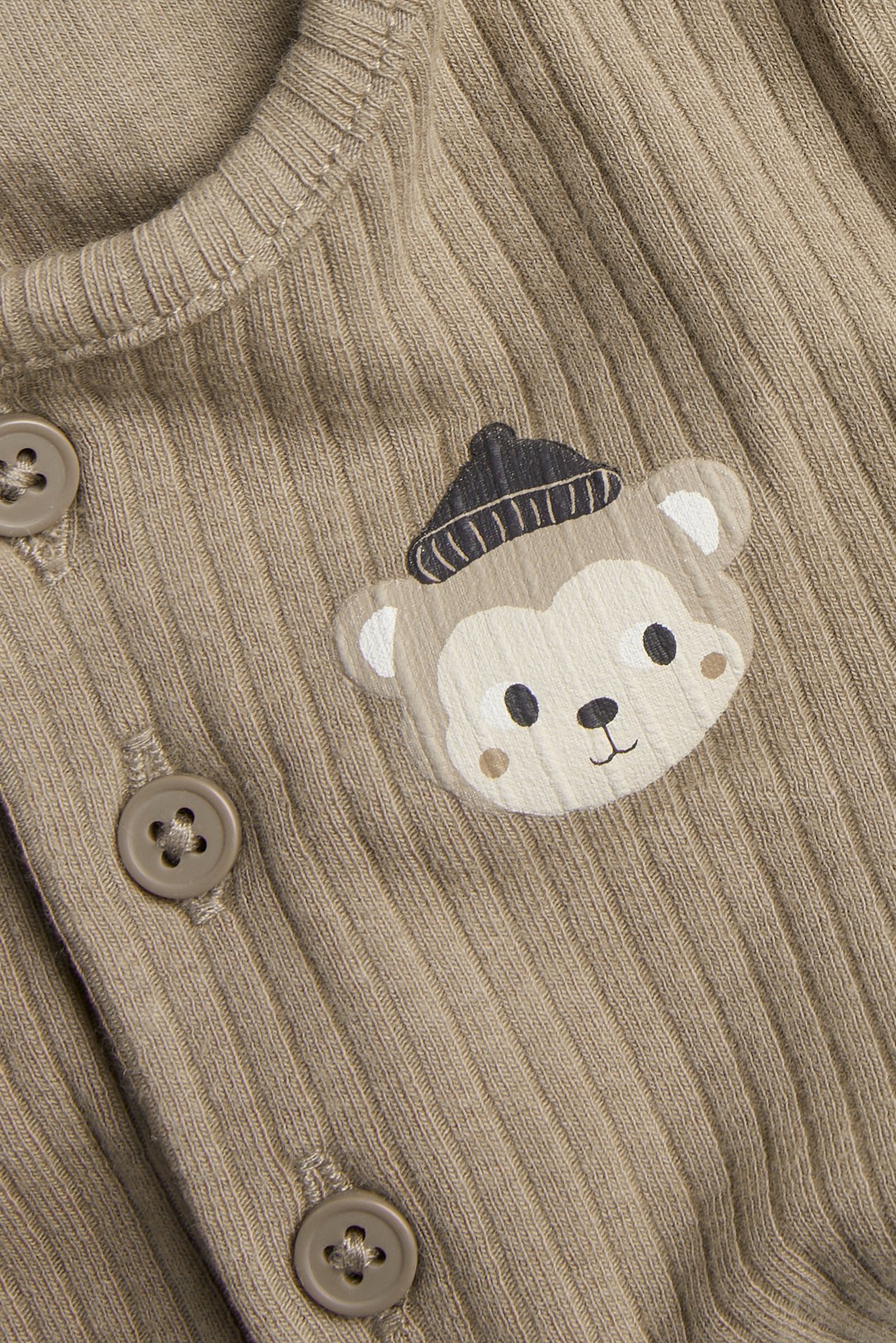 Närbild framifrån på en brun ribbad babybody med apträck och bruna knappar.