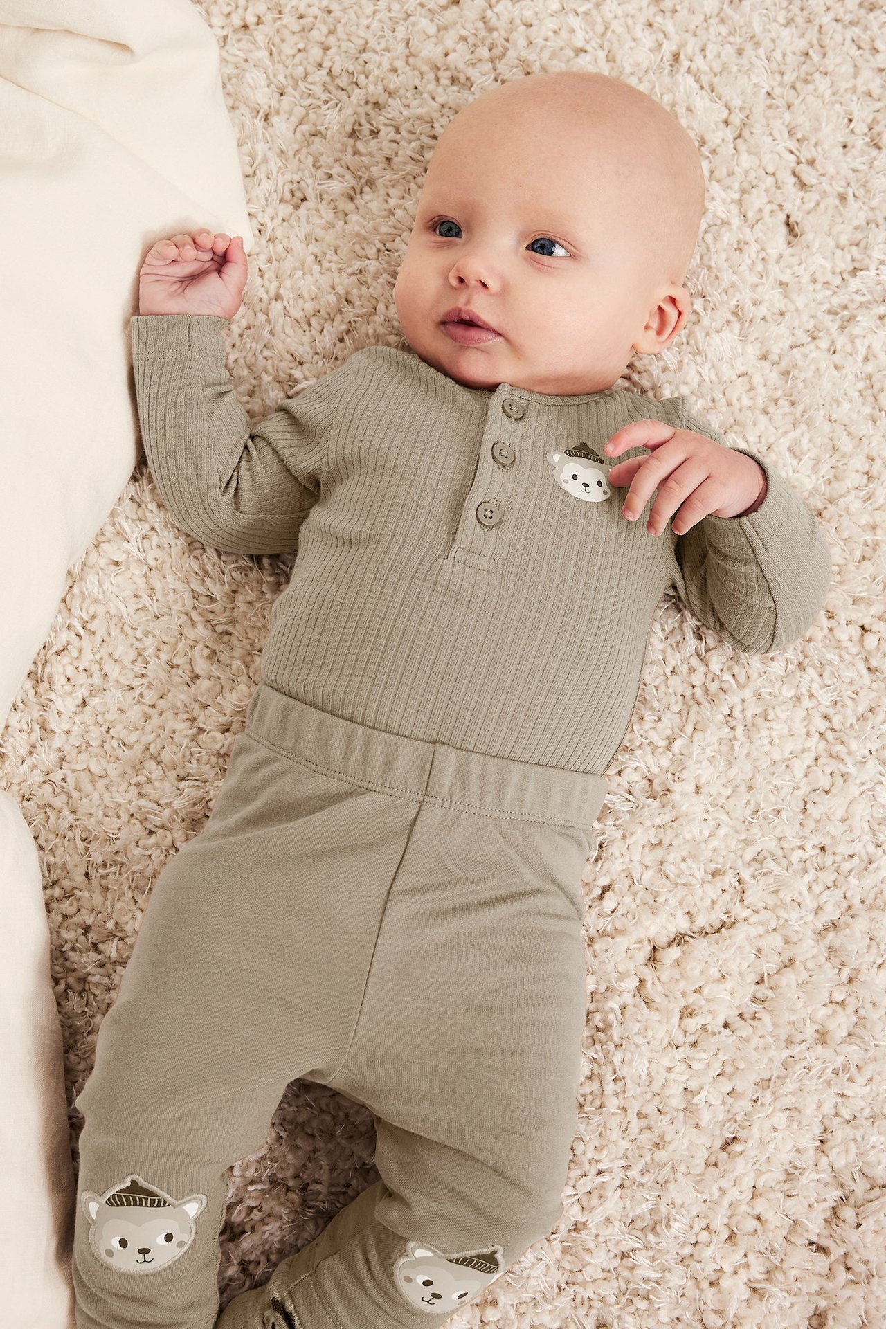 Ovenfra bilde av en baby i en lys brun ribbet langermet body med trykk og matchende mønstrede leggings.