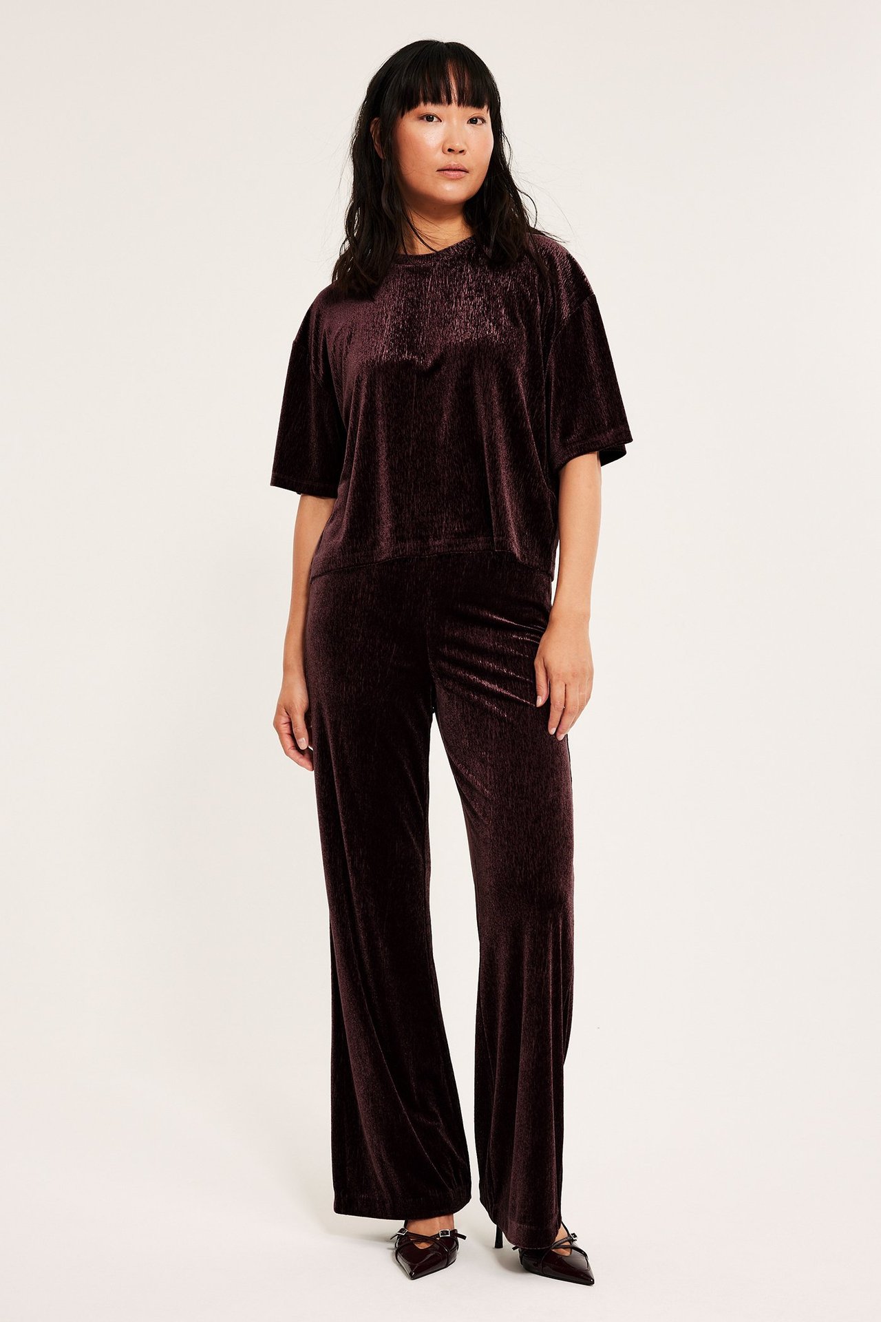 Kvinne i vinrød, løs passform velour-topp med korte ermer og matchende velourbukser.