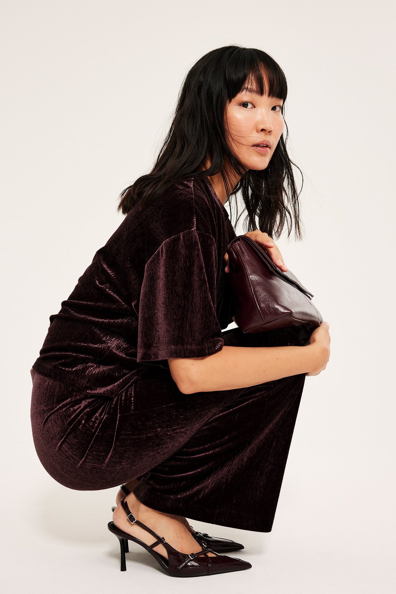 Vinrød velour topp med løs passform, kort erm, kvinne knørt ned, holder veske.