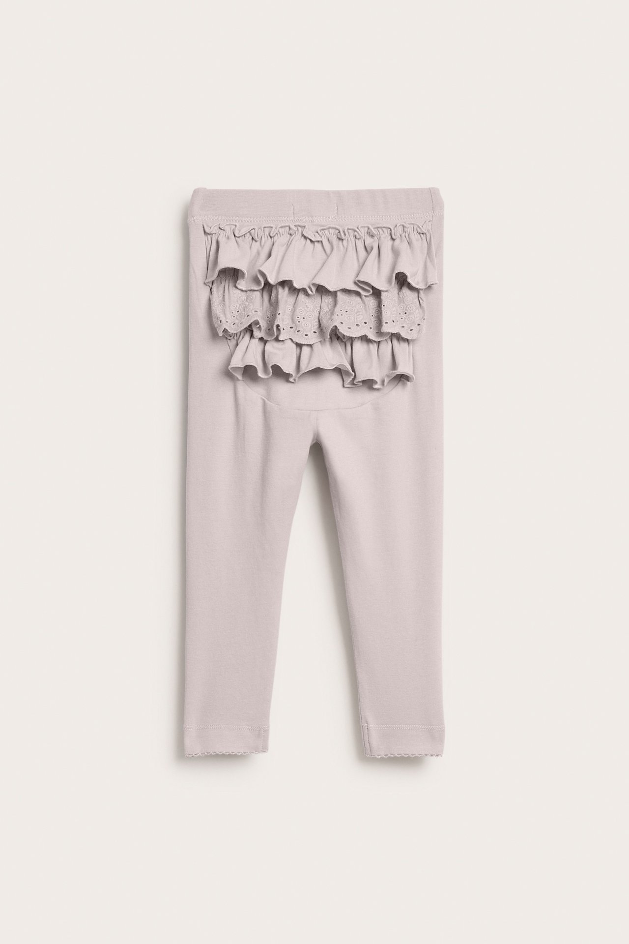 Bakfra av lysegrå baby-leggings med broderte volanger og bølgete kanter.