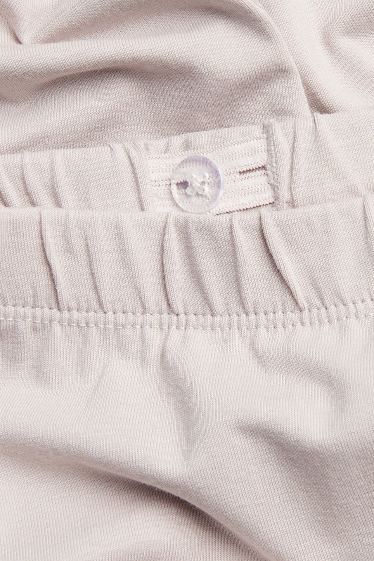 Zbliżenie jasnofioletowych bawełnianych legginsów, paska z regulowaną gumką i przezroczystym guzikiem.