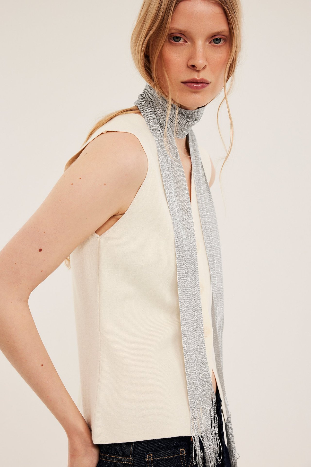 Nainen edestä hopeaglitterhuivi hapsuilla, stailattu luonnonvalkoisen hihattoman topin päällä.