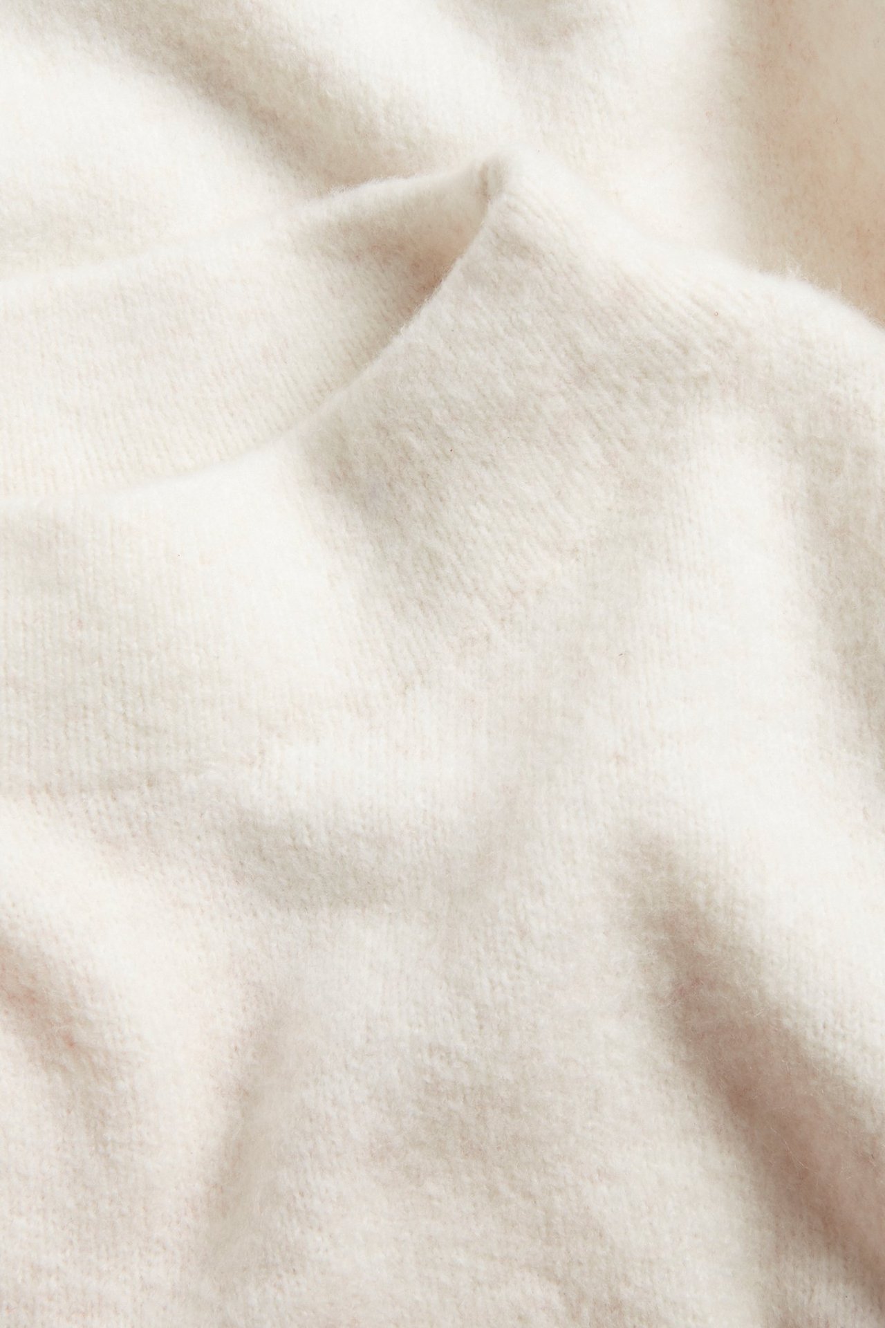 Närbild av mjukt, melerat vitt stickat tröjtyg med texturerad yta.