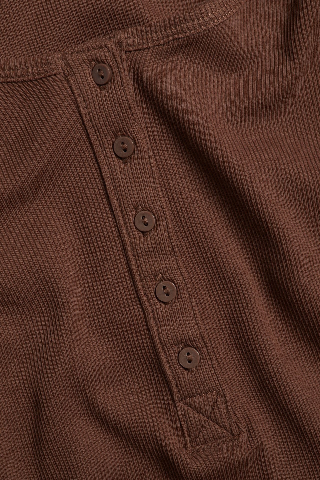 Zbliżenie brązowego prążkowanego topu z listwą guzikową z przodu i pięcioma brązowymi guzikami.