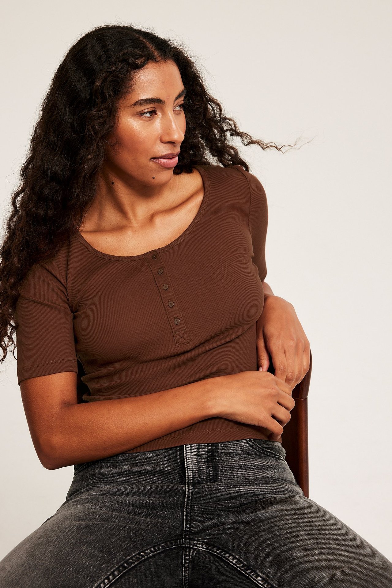 Kobieta w brązowym prążkowanym topie z guzikiem z przodu, siedzi, krótki rękaw, fakturalny materiał.